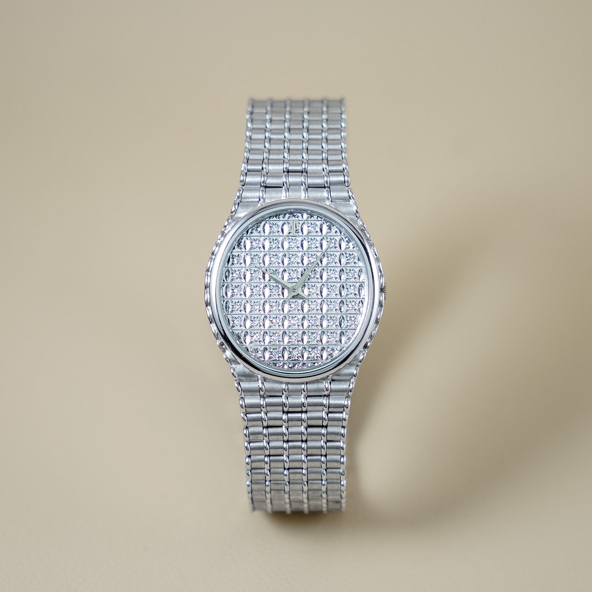 A silver-tone women's watch with a textured, diamond-encrusted dial and a matching link bracelet, centered on a warm beige background.