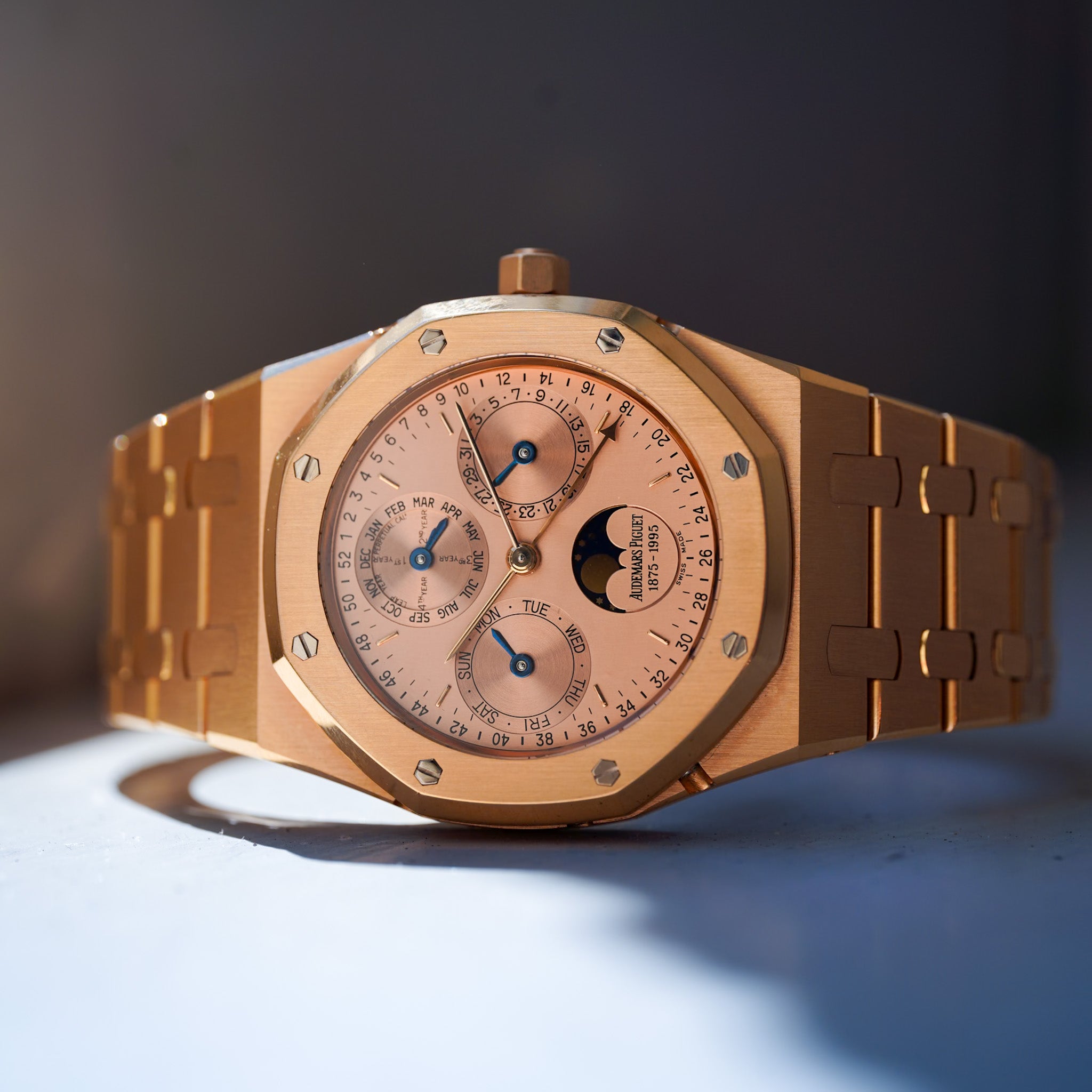 A luxury rose gold watch with an octagonal bezel, matching rose gold bracelet, and a light pink dial featuring three sub-dials and a moon phase indicator.