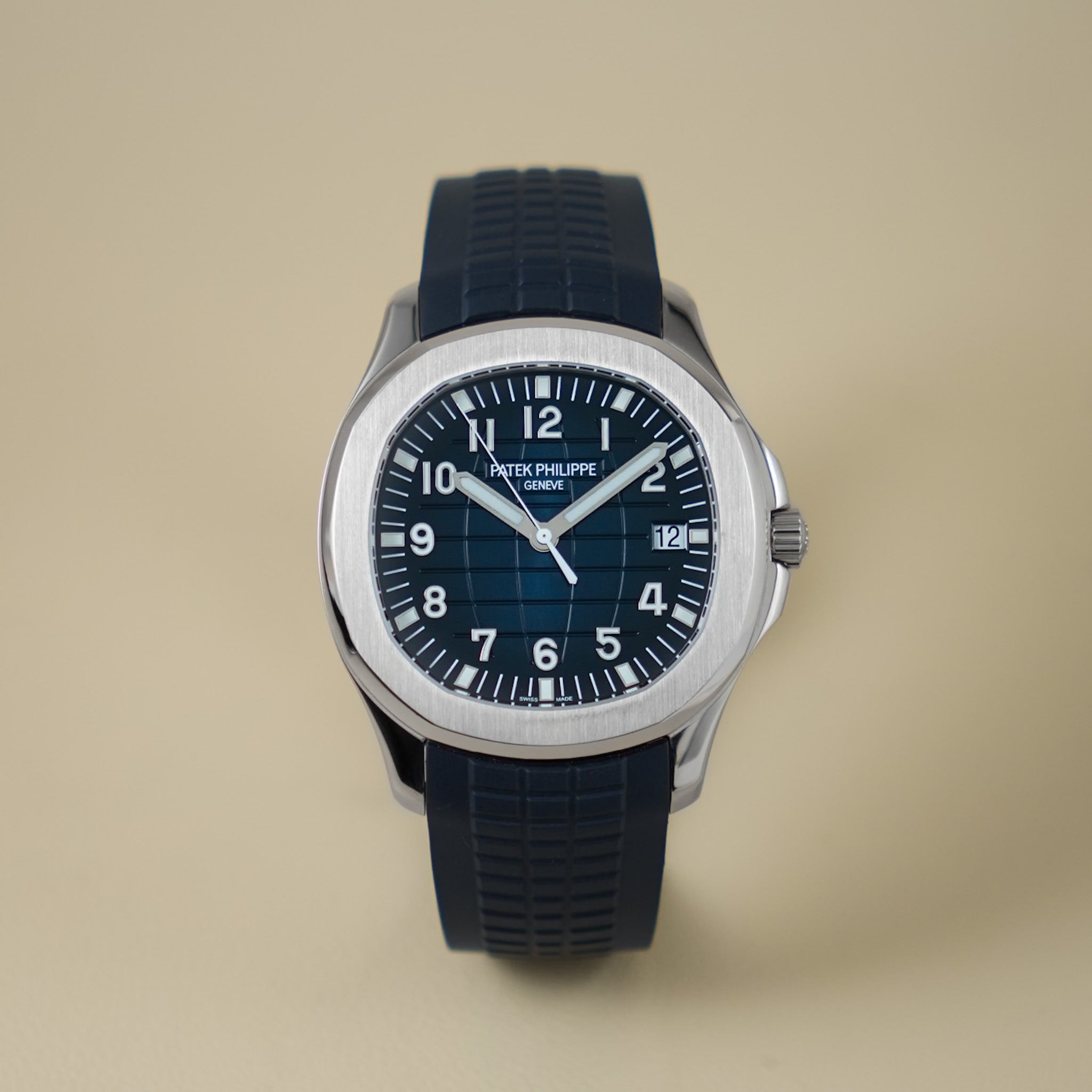 A Patek Philippe Aquanaut with a white gold case, blue dial, and blue textured rubber strap, shot against a neutral cream background.