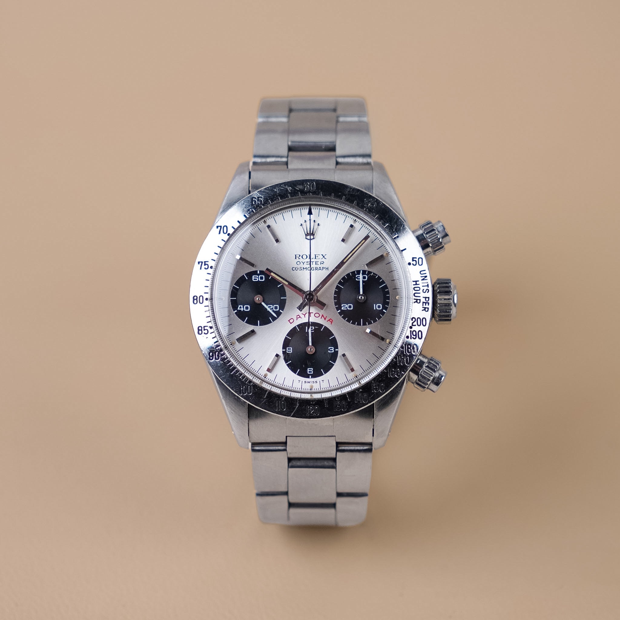 A vintage Rolex chronograph watch with a steel case, steel bezel, silver dial with black subdials, and a steel bracelet, shot upright against a solid beige background. 