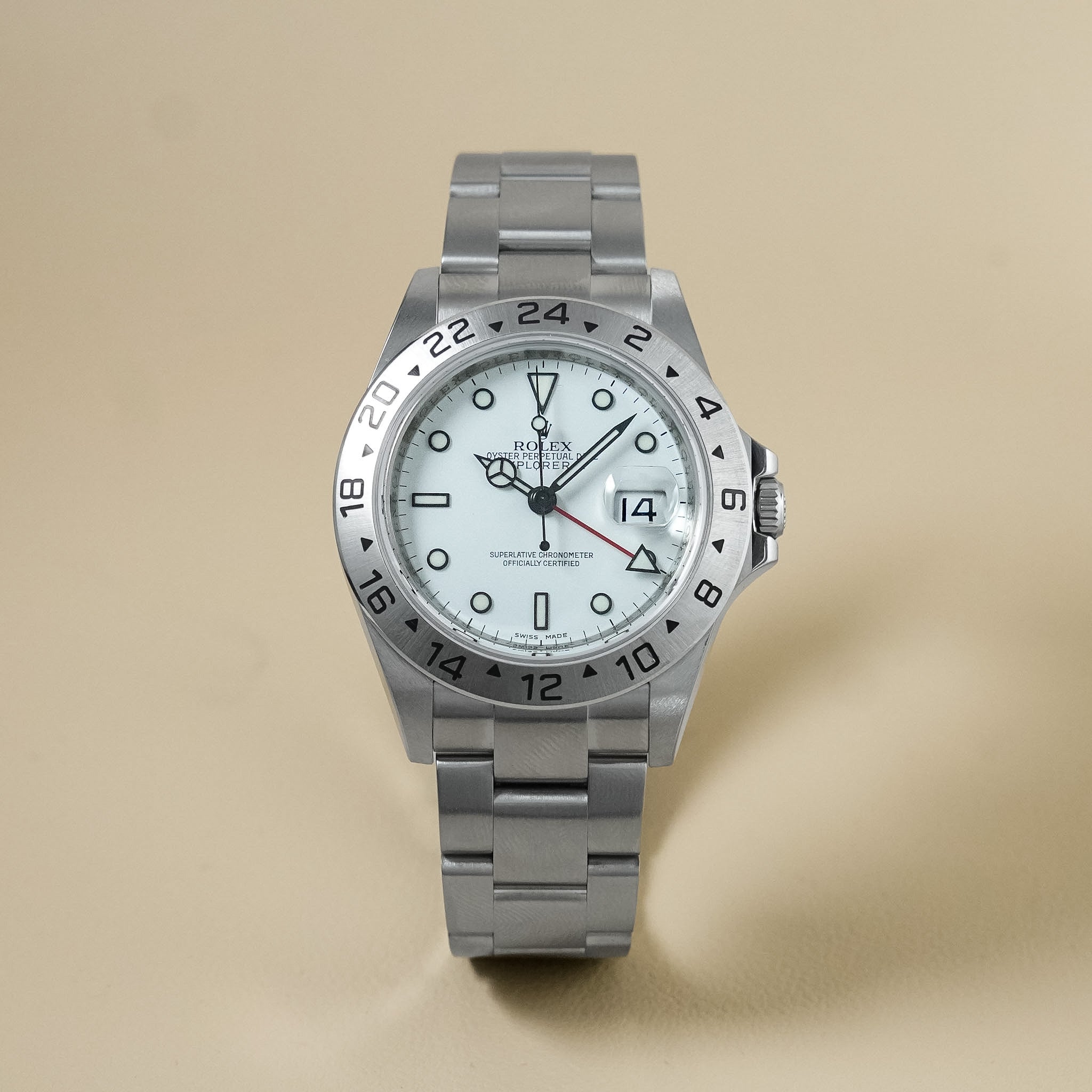 Rolex Explorer II watch with a stainless steel Oyster bracelet, featuring a white dial, steel bezel with black markings, and date window, set against a solid beige background.