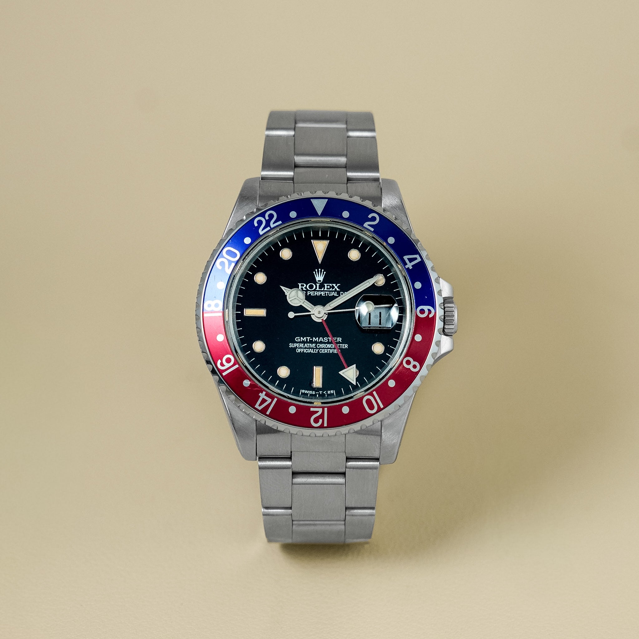 Rolex GMT-Master watch with a stainless steel Oyster bracelet and a two-tone blue and red bezel, shown against a solid beige background.