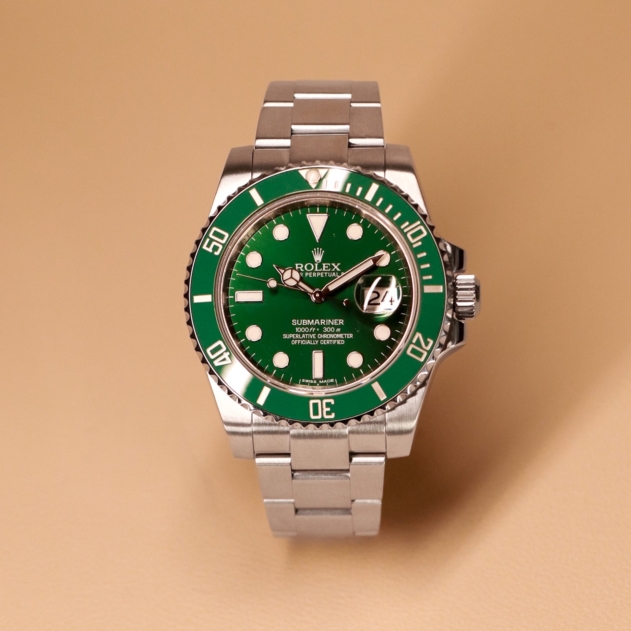 Rolex watch with green dial and silver metal bracelet on a beige background