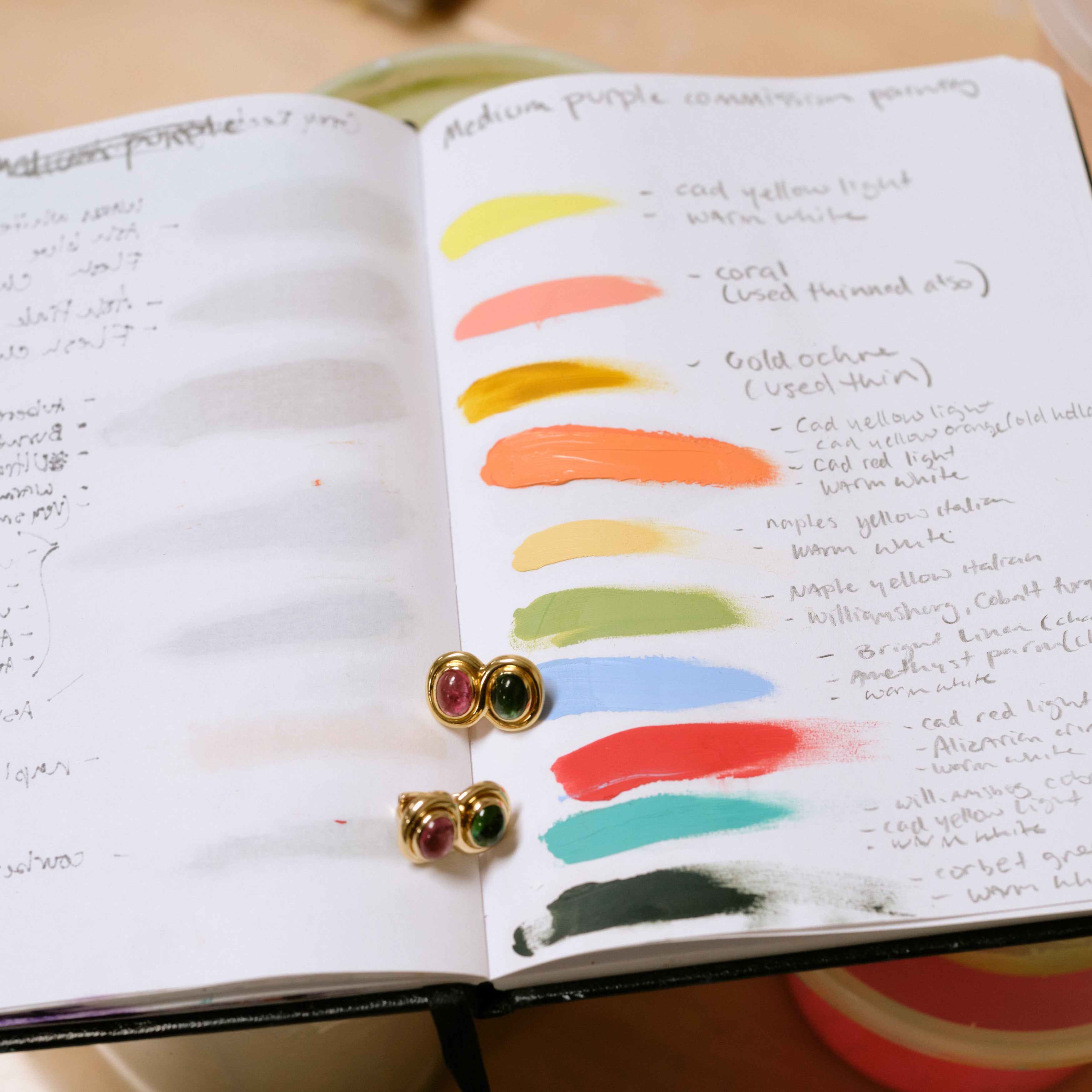Vintage Bvlgari pink and green tourmaline earrings resting on an open sketchbook page of hand-painted color swatches