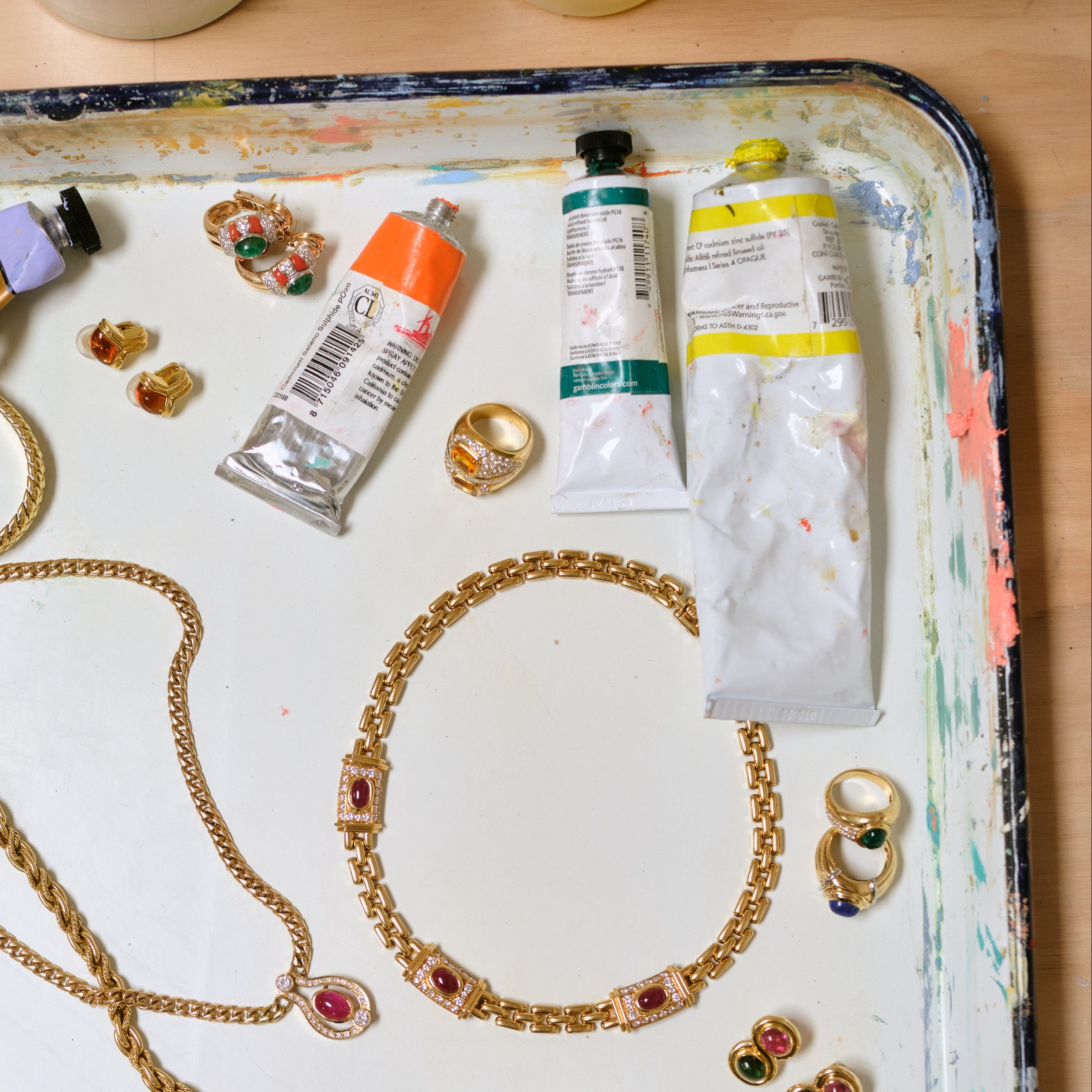Vintage Cartier ruby and diamond necklace resting on a paint-splattered tray alongside other gold vintage jewelry