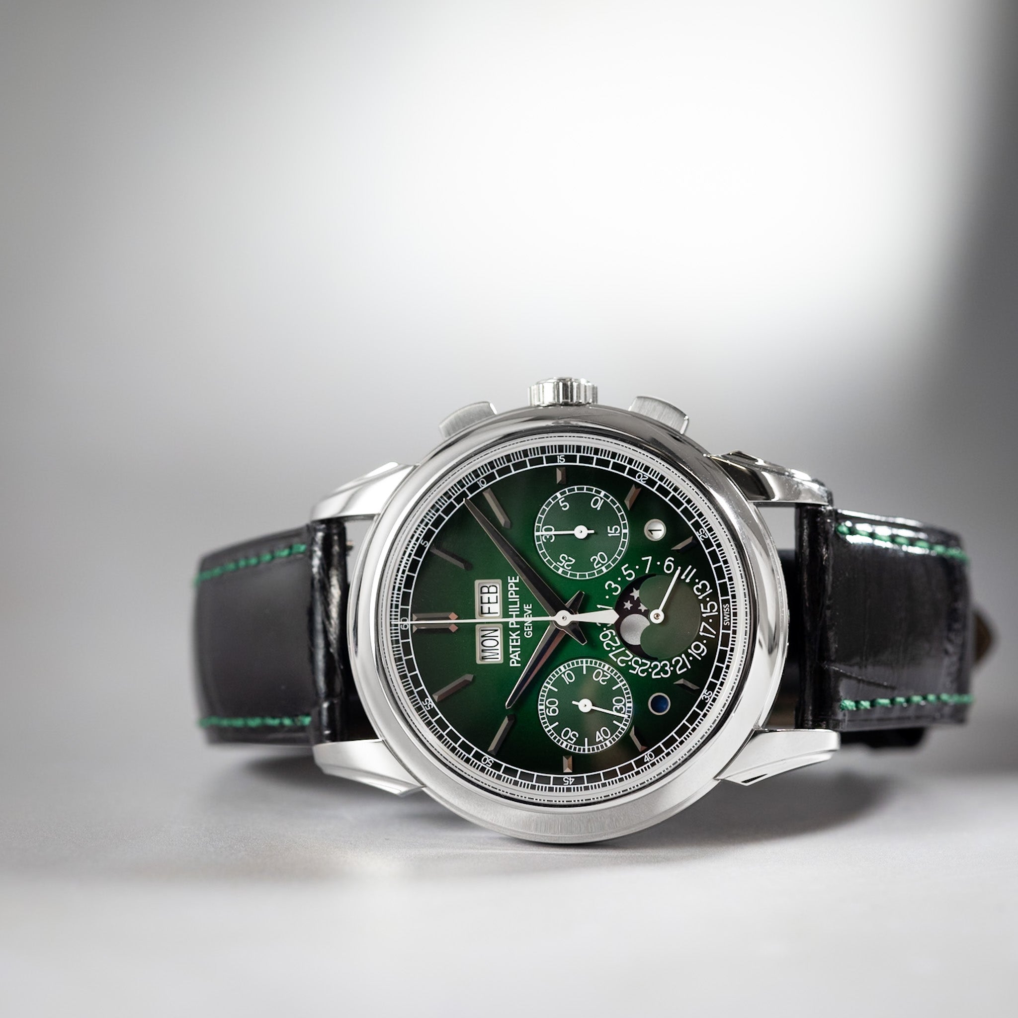 Wristwatch with green face and black leather strap on a gray background