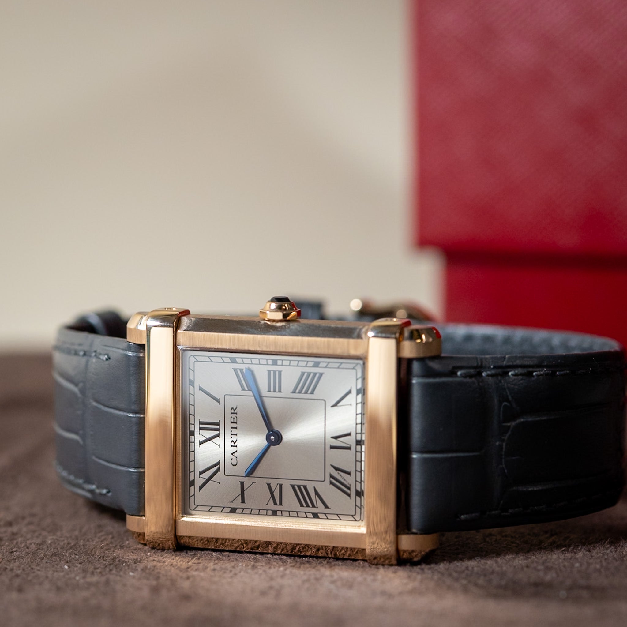 Cartier watch with black leather strap and gold case on a textured surface