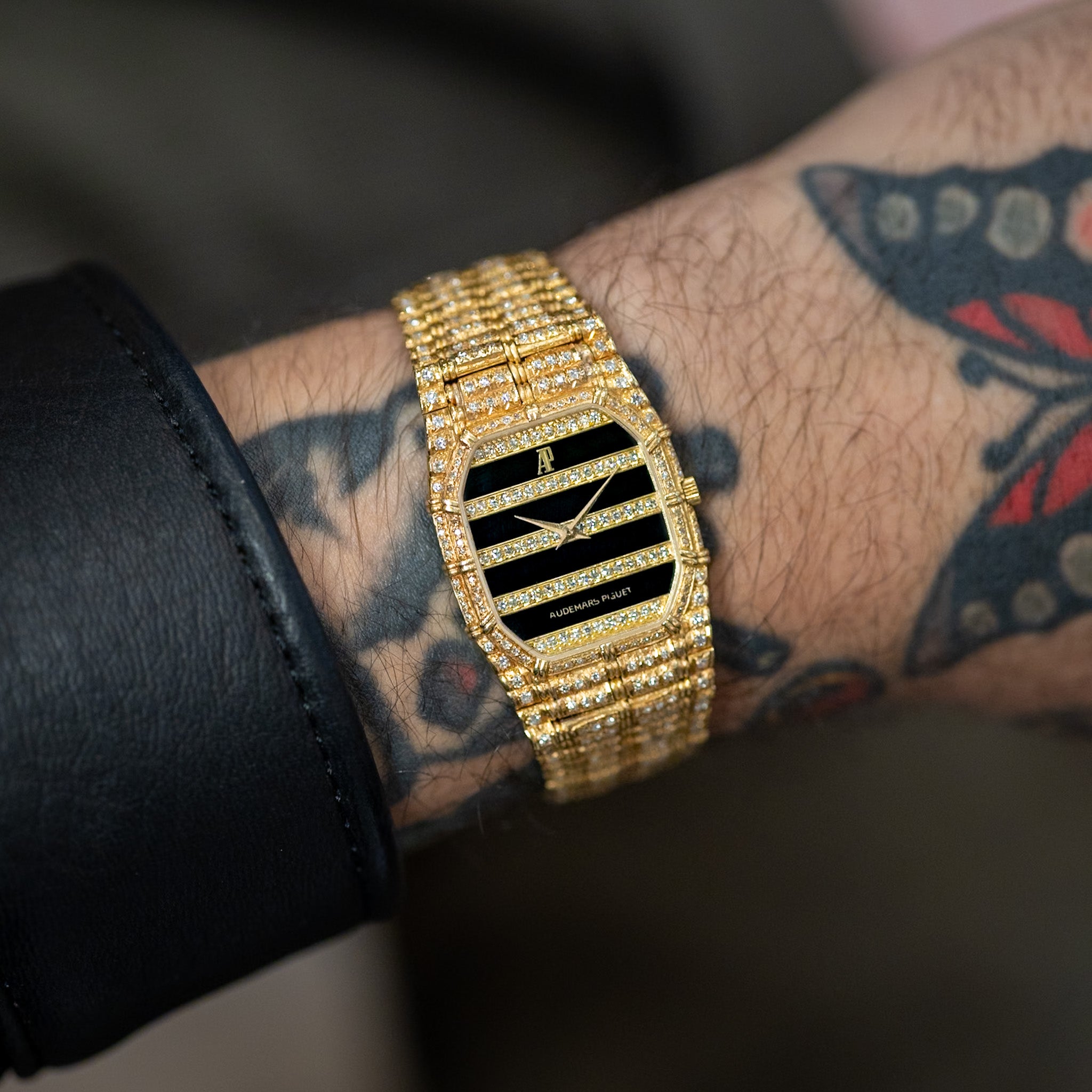 Gold watch with black face on a wrist with tattoos