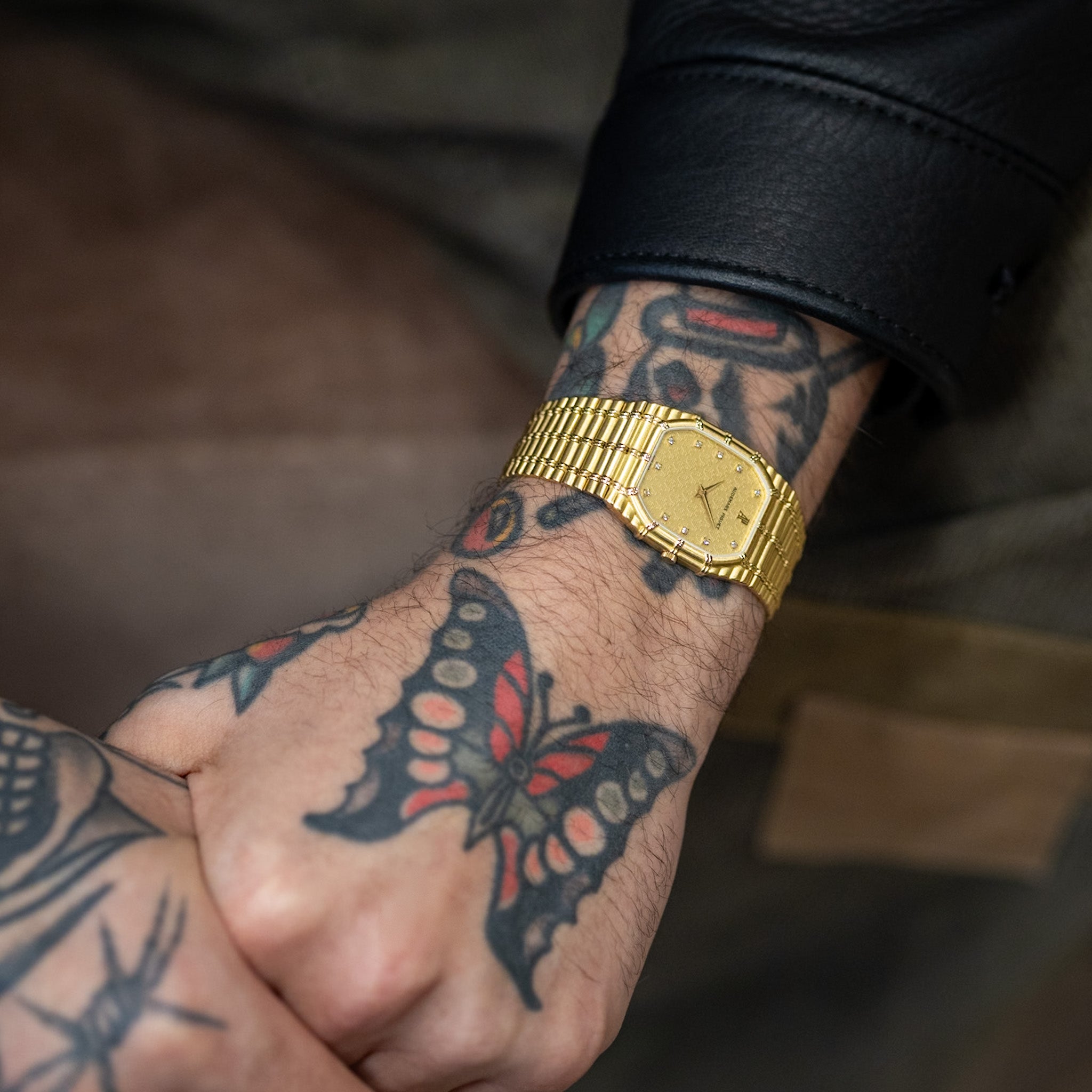 Gold wristwatch on a tattooed wrist with a blurred background
