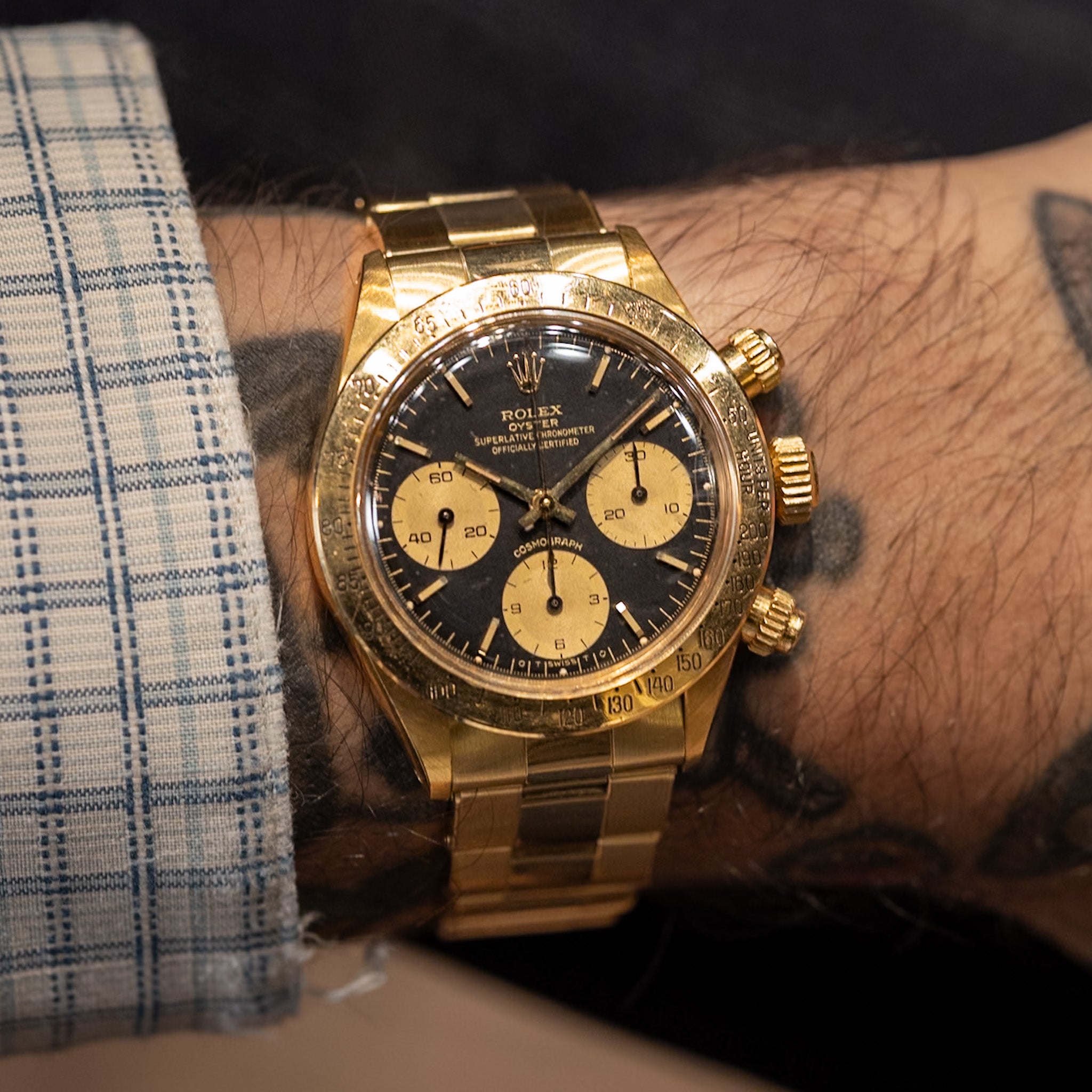 Gold Rolex watch on a wrist with a checkered sleeve