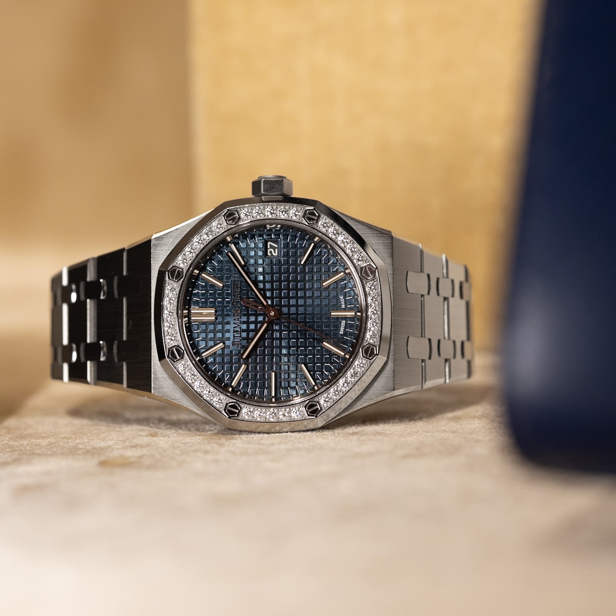 Luxury watch with a metallic band and blue face on a beige surface