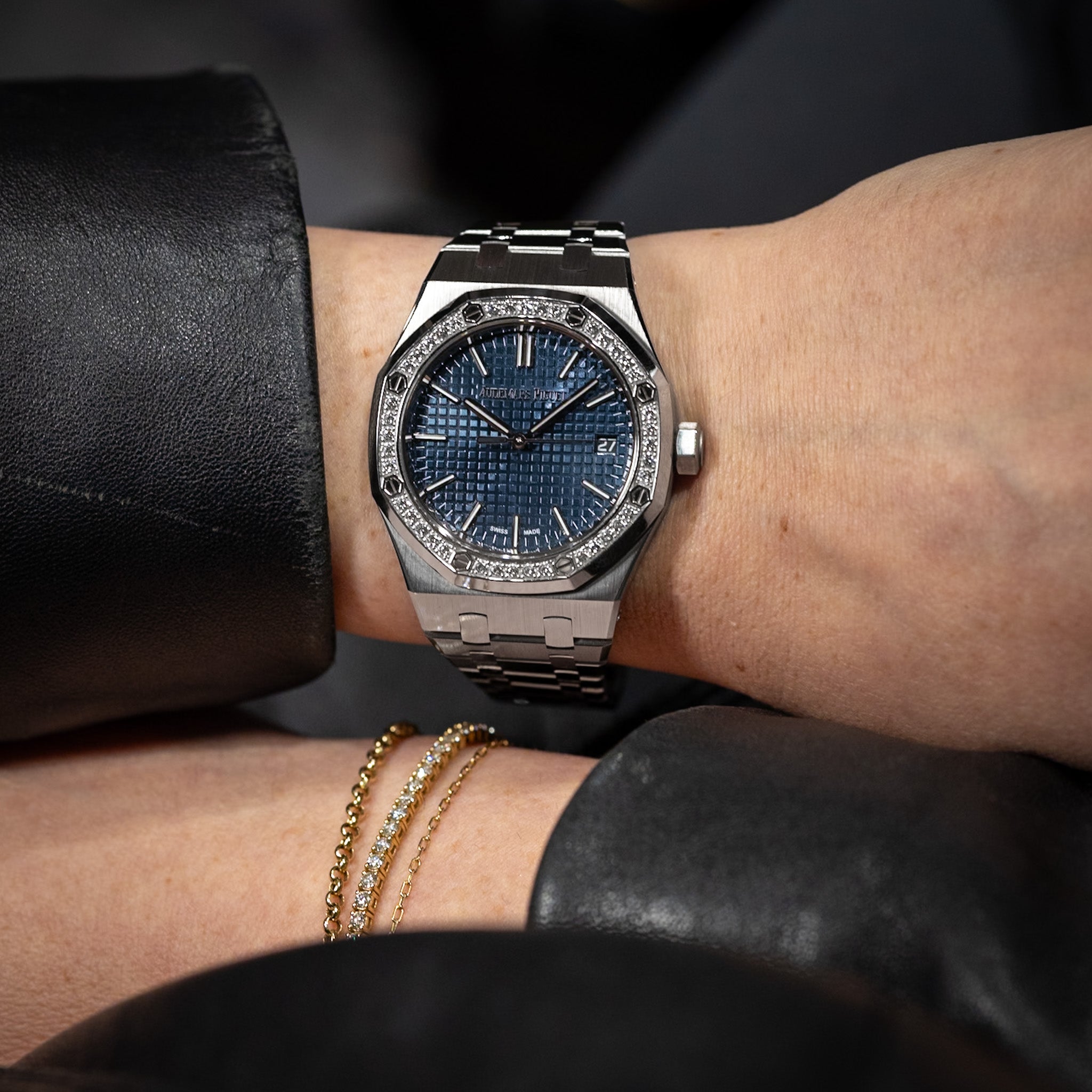 Luxury watch with blue face and diamond accents on a wrist, with a blurred background.