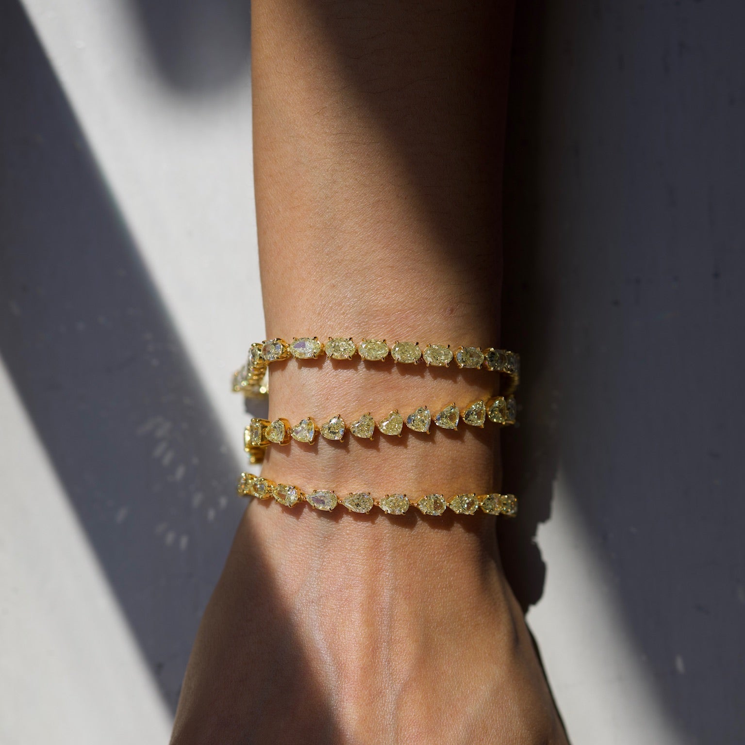 Hand wearing multiple gold bracelets on a neutral background