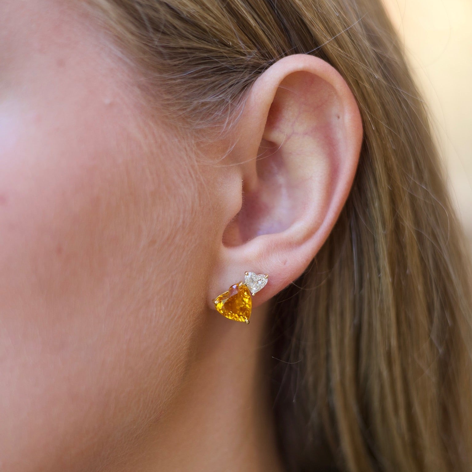 Close-up of a person wearing a heart-shaped yellow gemstone earring.