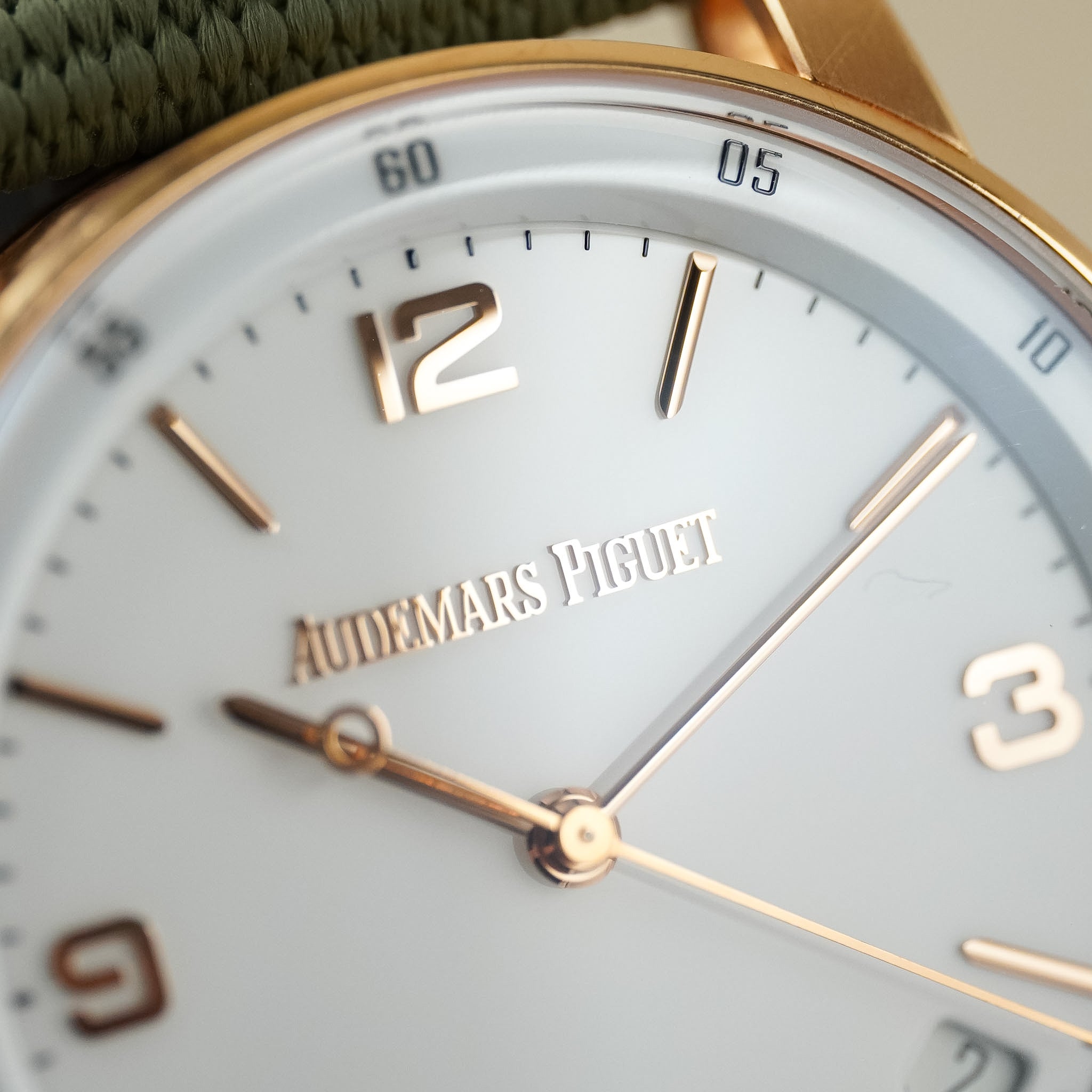 Close-up of an Audemars Piguet watch dial with a pale blue face, gold-tone bezel and hands, and a green woven strap visible at the top.