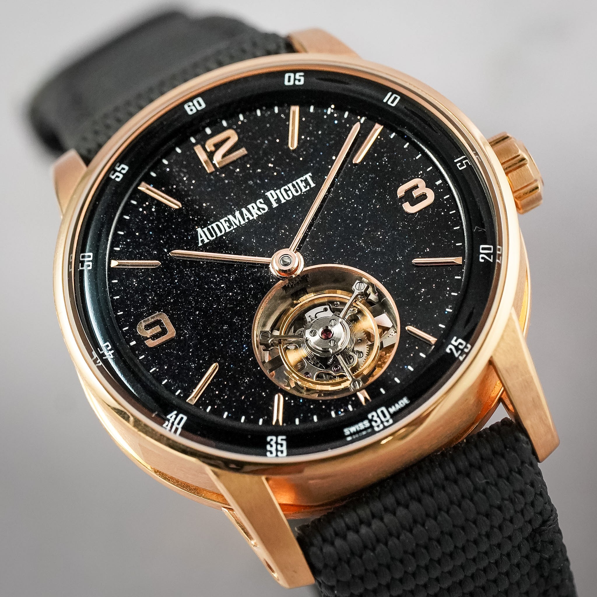 A close-up shot of a Audemars Piguet Royal Oak watch featuring a black starry dial, a gold-tone case, and a black fabric strap.