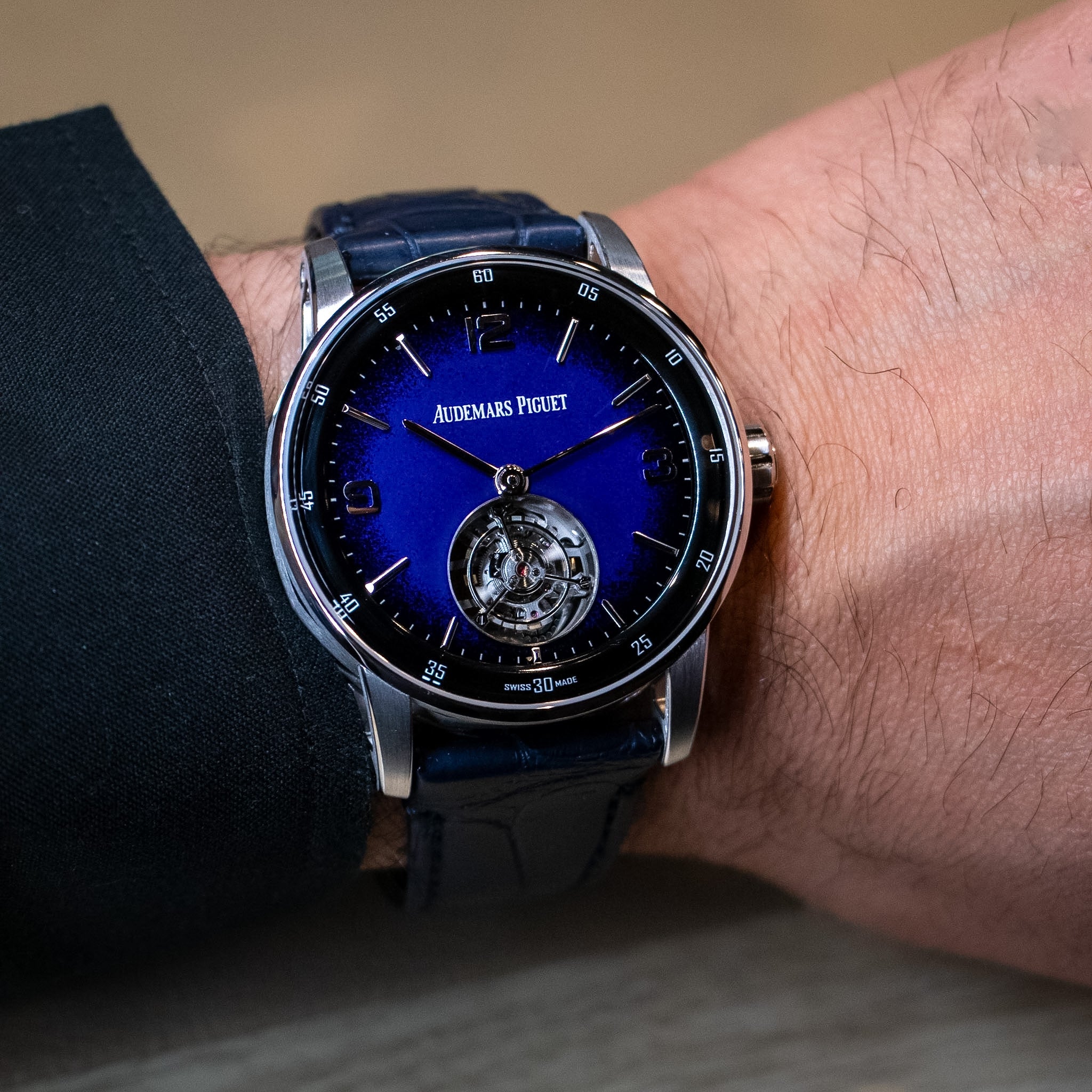 A close-up of a wrist wearing an Audemars Piguet watch with a deep blue dial, blue leather strap, and silver-toned case.