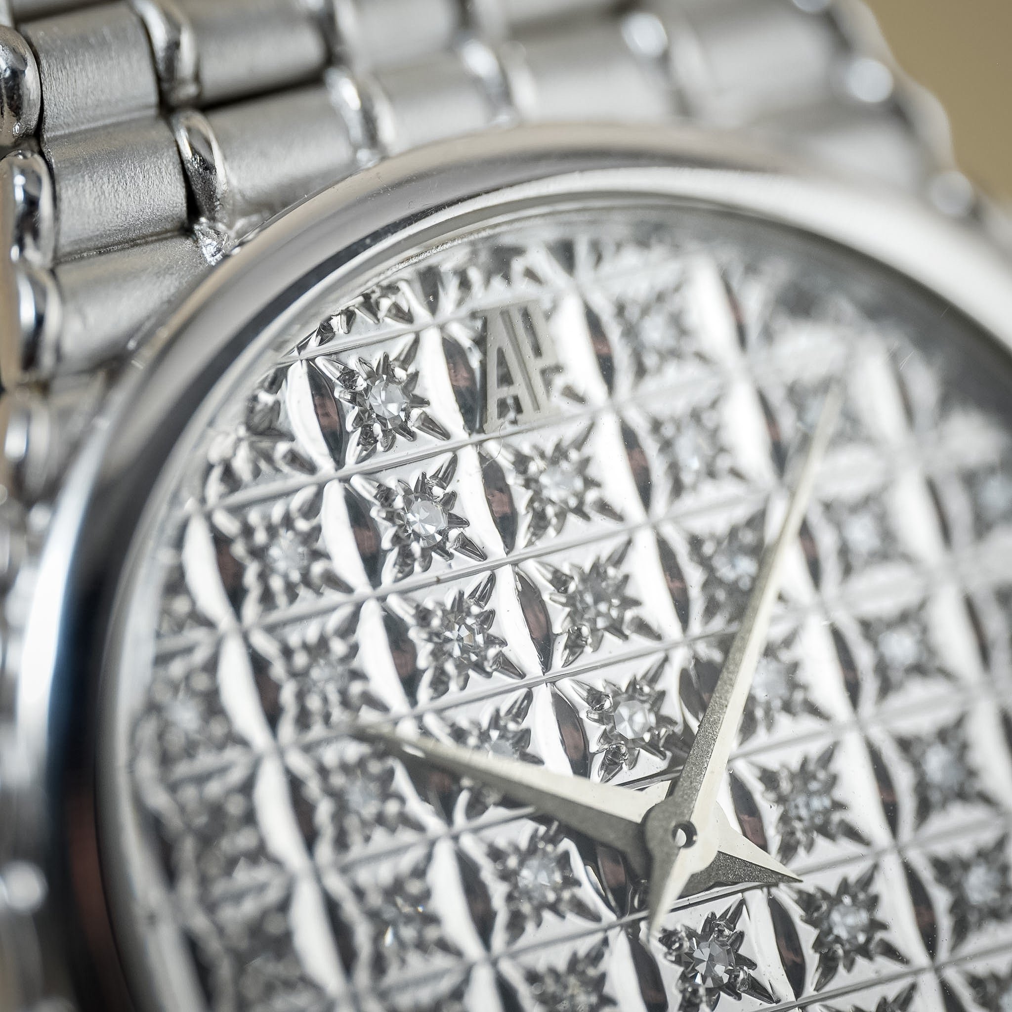 Close-up of a silver-toned wristwatch with a highly textured, patterned dial and matching metal bracelet.