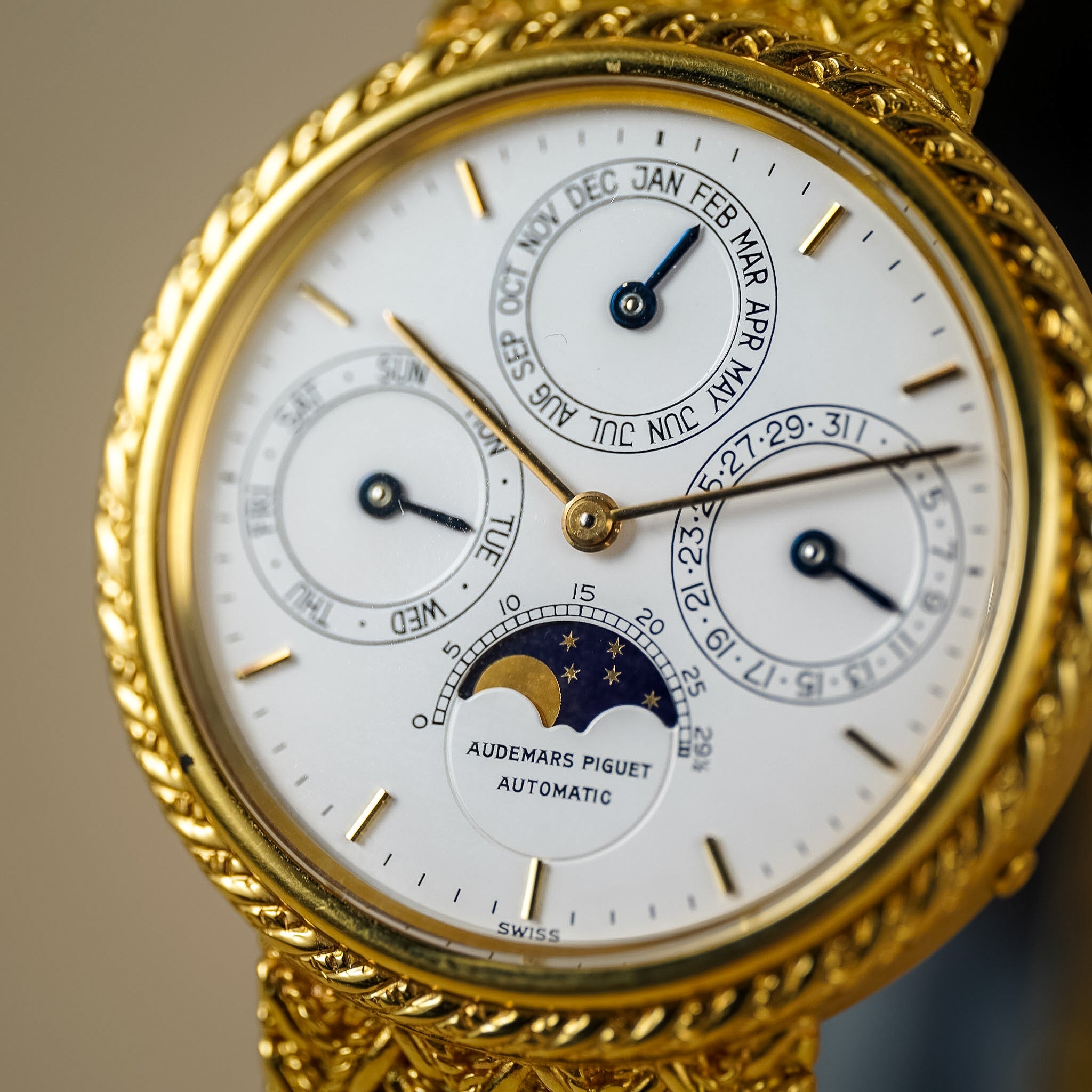 Close-up of an Audemars Piguet automatic watch with a white dial, gold-toned case, and ornate gold-toned rope-banded strap.