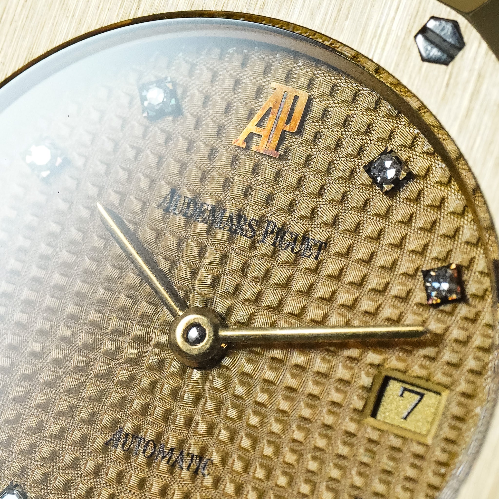 Close-up of an Audemars Piguet Automate watch dial, featuring a textured gold-tone patterned face, gold hands, diamond hour markers, and an AP logo at the 12 o'clock position.
