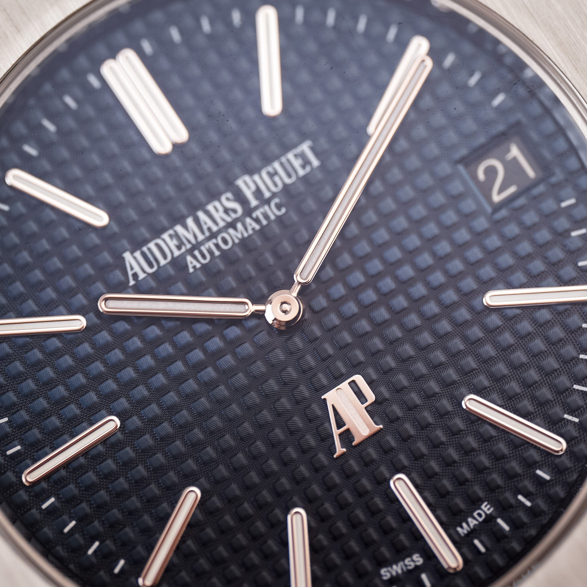 Closeup of a steel Audemars Piguet Royal Oak with a steel bezel, textured blue dial with a date window showing "21". The Audemars Piguet logo is visible.