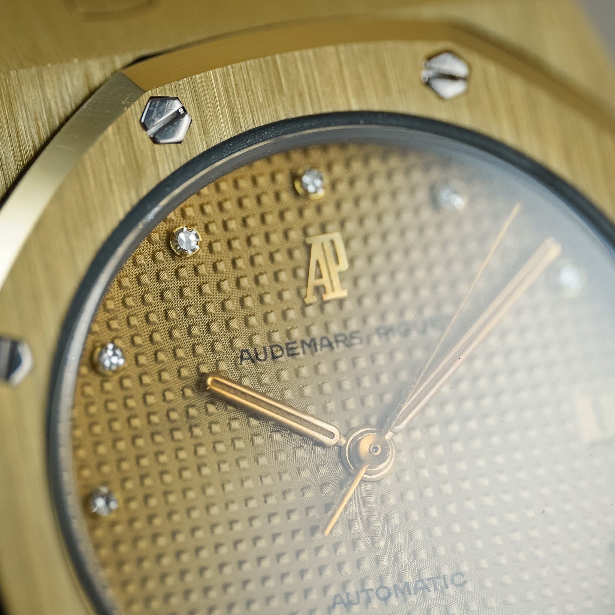 Close-up of an Audemars Piguet Royal Oak Automatic watch with a textured gold dial and gold bezel, featuring crystal hour markers and gold hands.