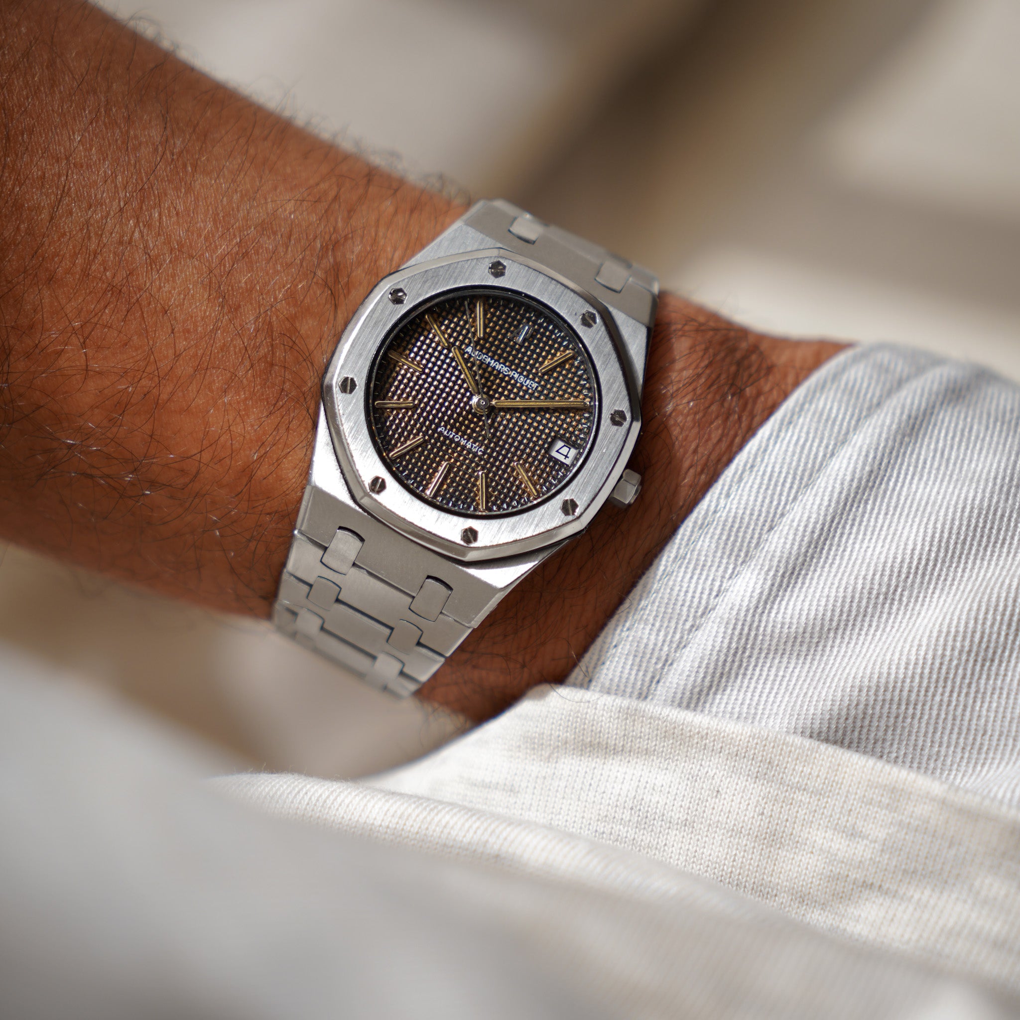 A silver-toned stainless steel wristwatch with a textured dark brown dial and octagonal bezel, shown worn on a person's wrist.