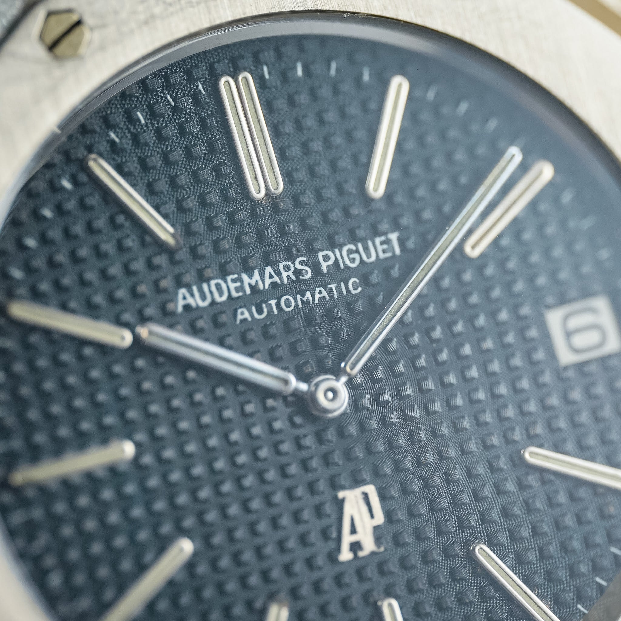 Close-up of an Audemars Piguet Automatic watch dial, showing a textured dark blue textured face with silver-tone stick indices and hands.