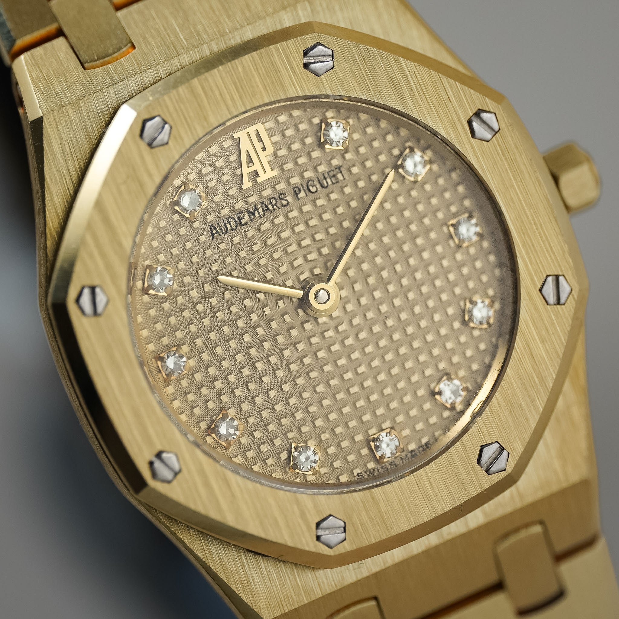 Close-up of an Audemars Piguet Royal Oak watch with a brushed gold-tone case, diamond hour markers, and a textured gold dial.