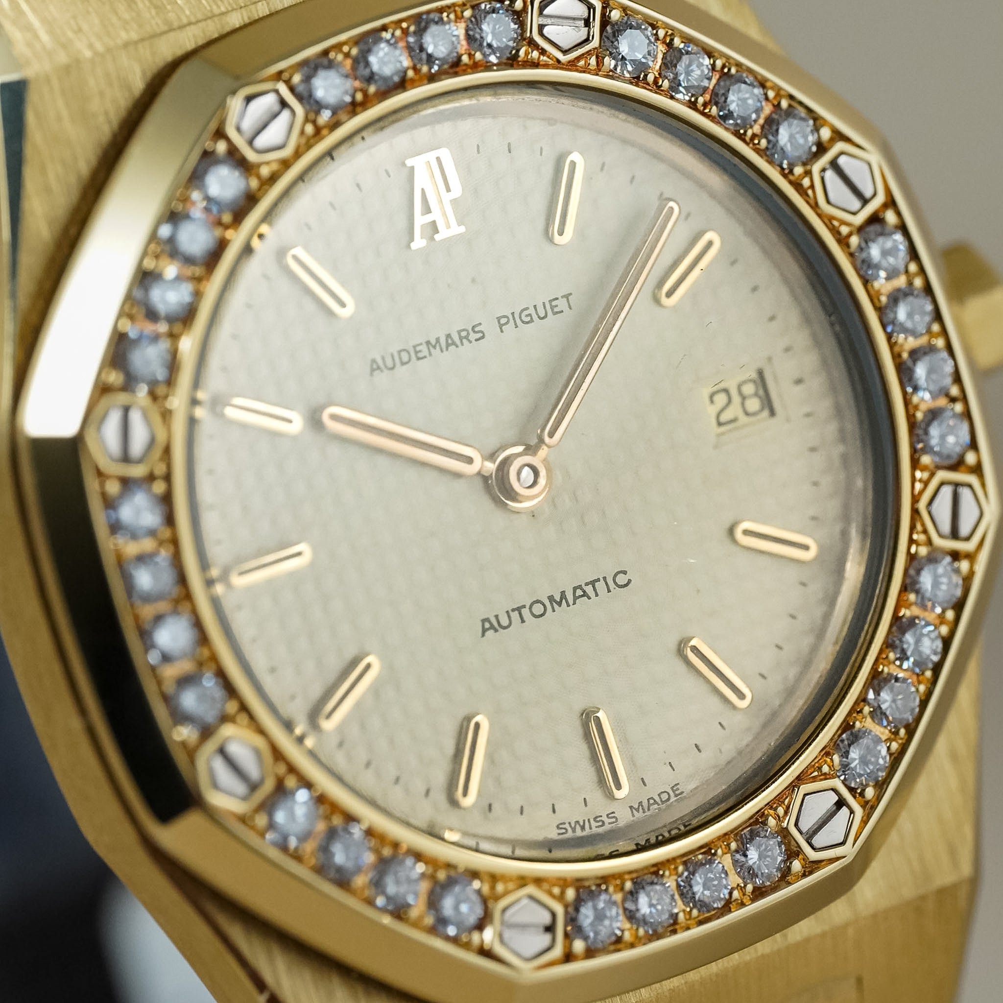 Close-up of an Audemars Piguet Royal Oak Automatic watch with a gold-toned case, diamond-set bezel, and champagne dial.