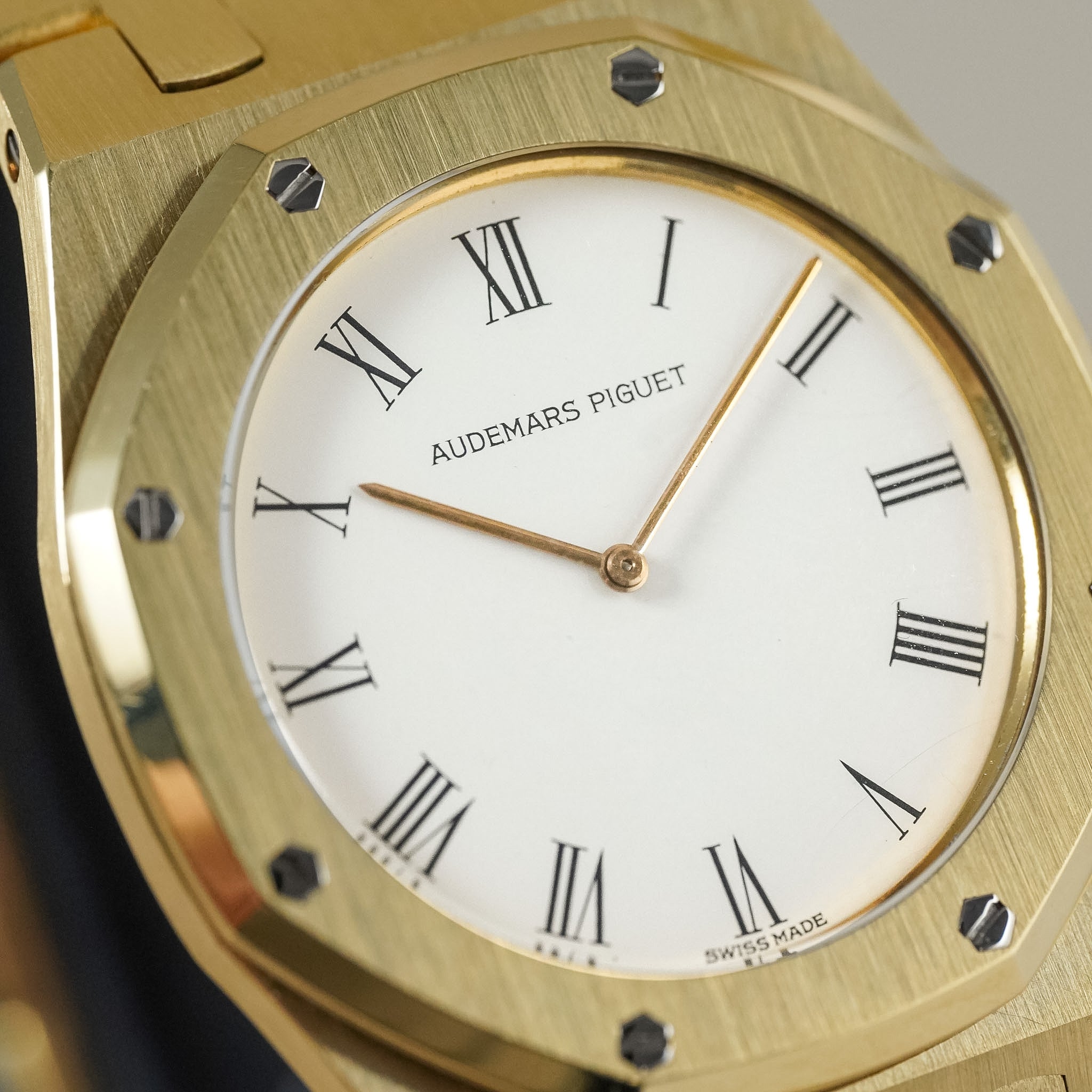Close-up of an Audemars Piguet Royal Oak watch with a gold-toned octagonal bezel, white dial, and black Roman numerals.