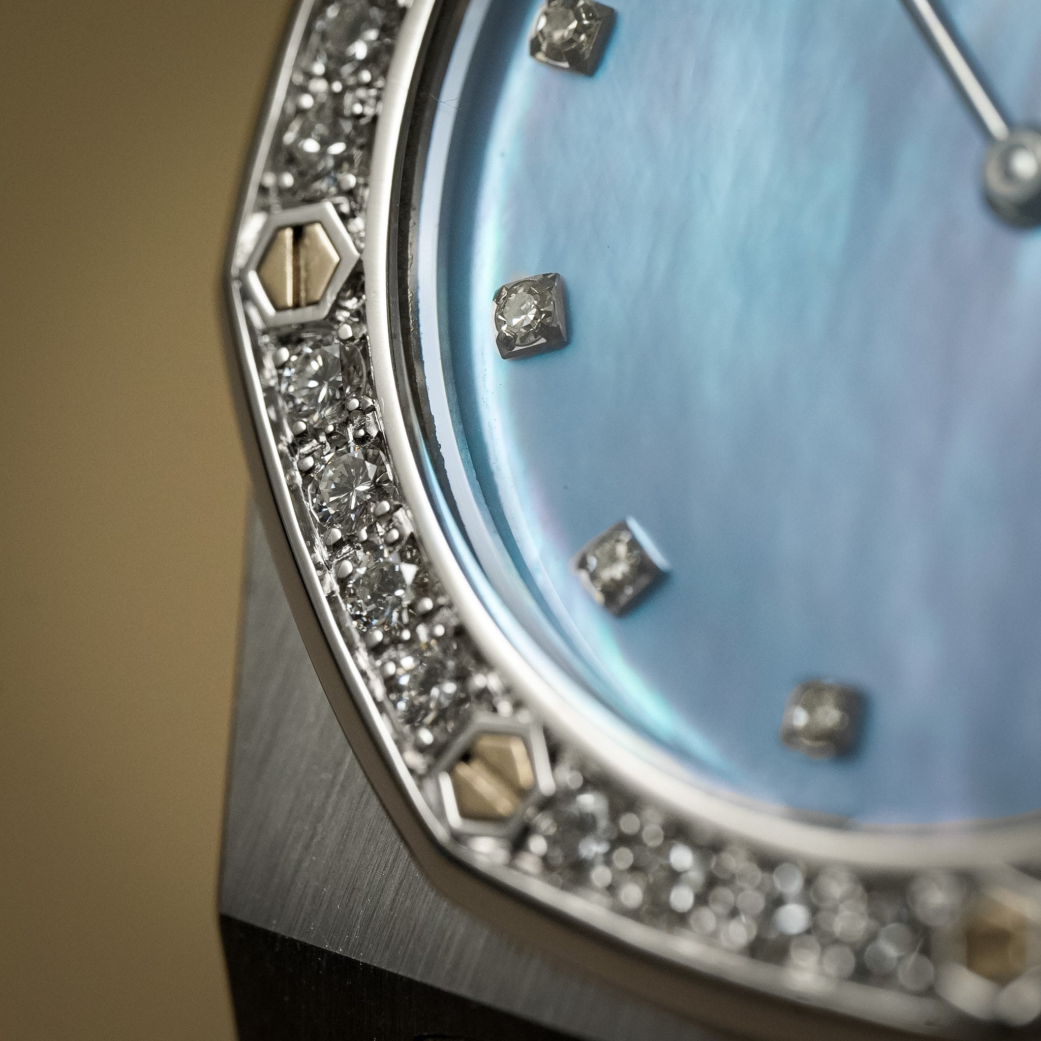 Closeup of a white gold Audemars Piguet Royal Oak with a mother of pearl dial, diamond bezel, and diamond hour markers. Shot against a neutral cream background.