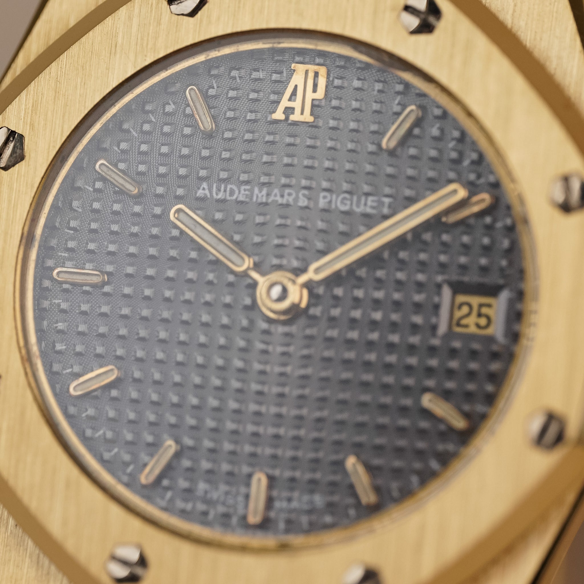 Closeup of an Audemars Piguet Royal Oak with a yellow gold case, yellow gold bezel, and a textured grey dial with a date window at 3 o'clock.