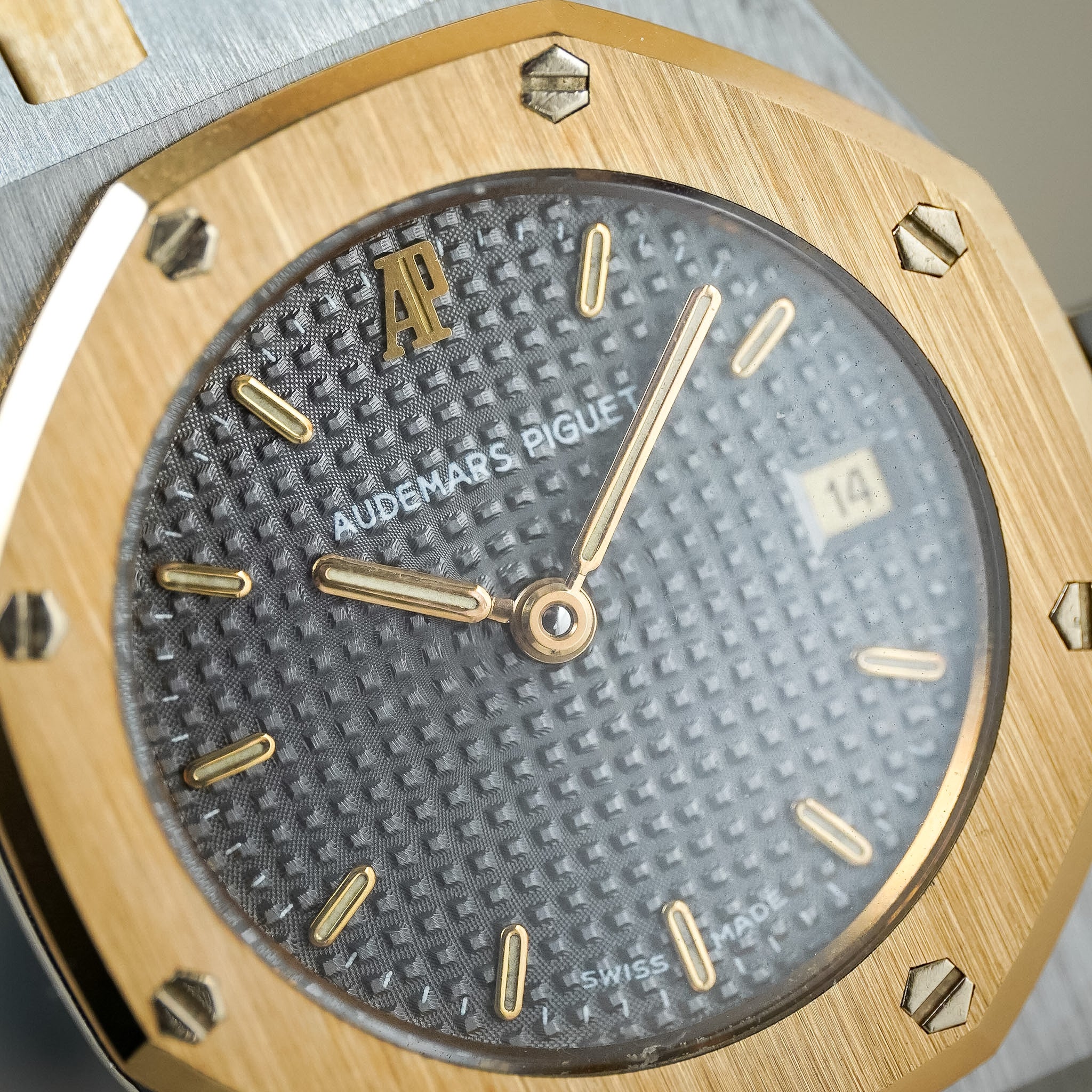 Close-up of an Audemars Piguet Royal Oak watch featuring a brushed gold-tone case, a textured dark gray dial, and gold-tone hour markers and hands.