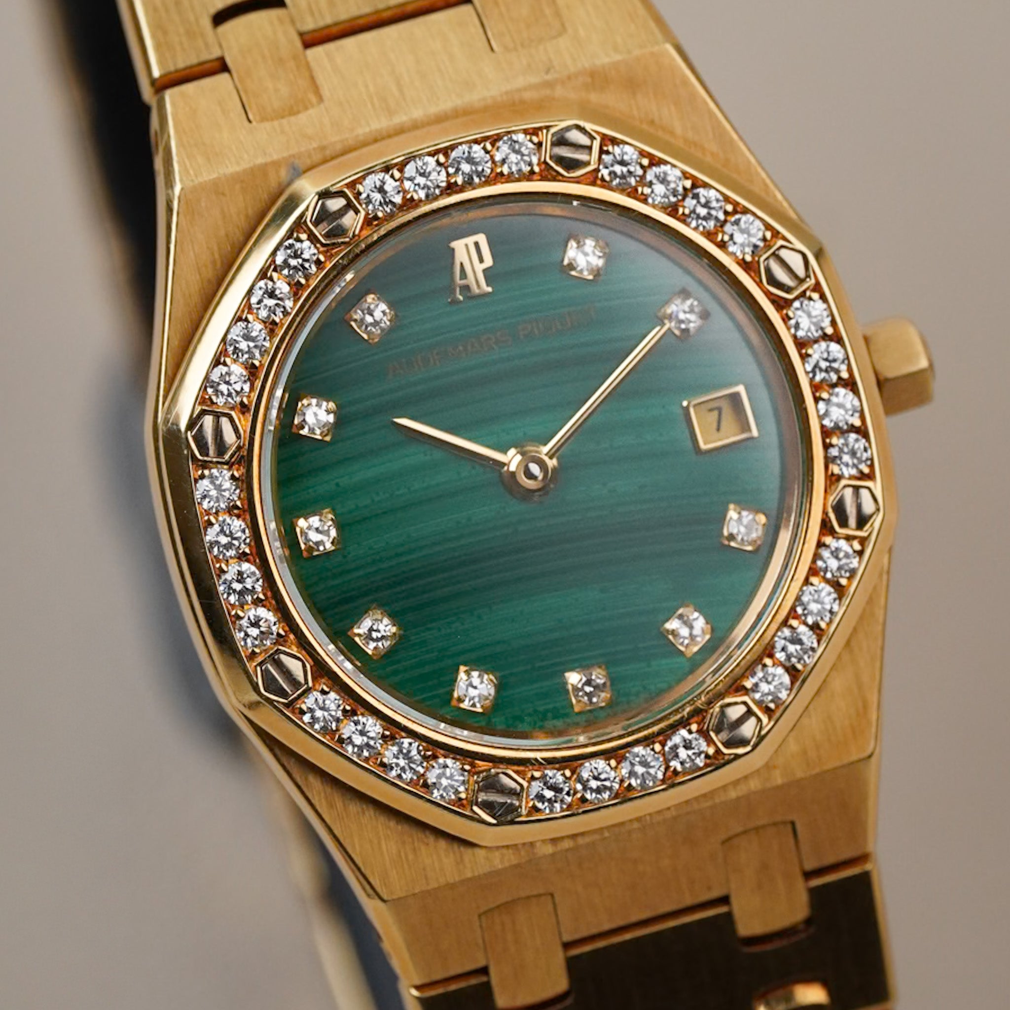 A ladies yellow gold Royak Oak with a malachite dial, diamond bezel and hour markers, and a date window, shot against a neutral grey background