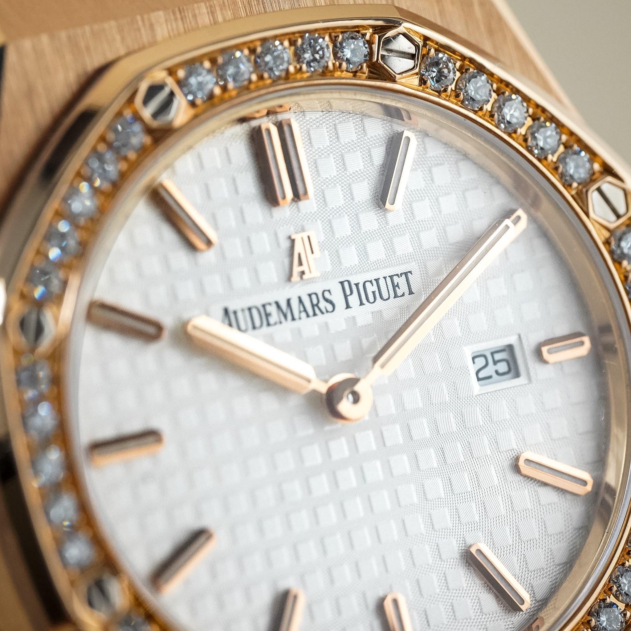 Close-up of an Audemars Piguet watch featuring a gold-toned case, a bezel set with clear crystals, and a white textured dial with gold-toned hour markers and hands.