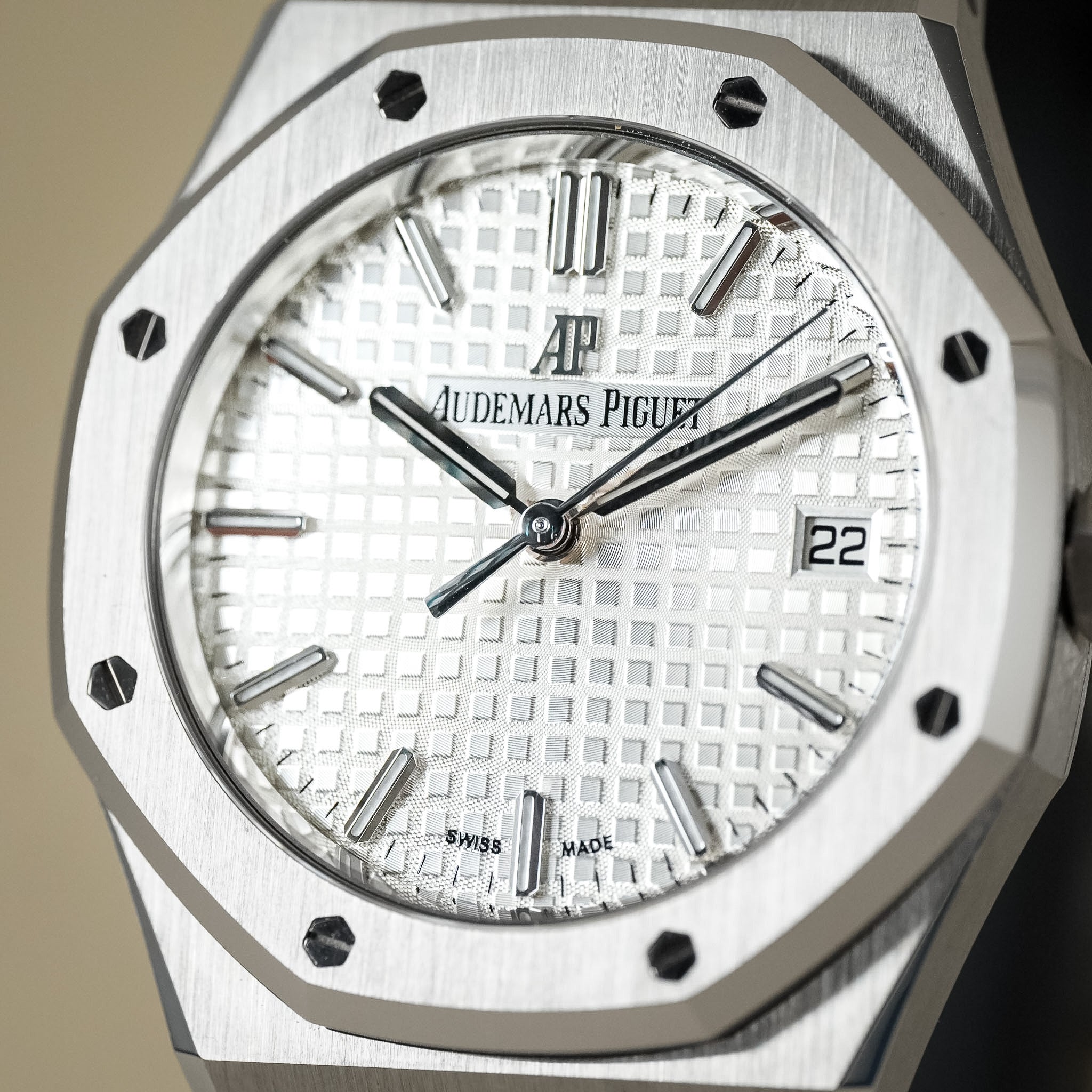 Close-up of an Audemars Piguet Royal Oak watch with a brushed silver-toned metal case, white textured dial, black hands and markers, and a date window at 3 o'clock.