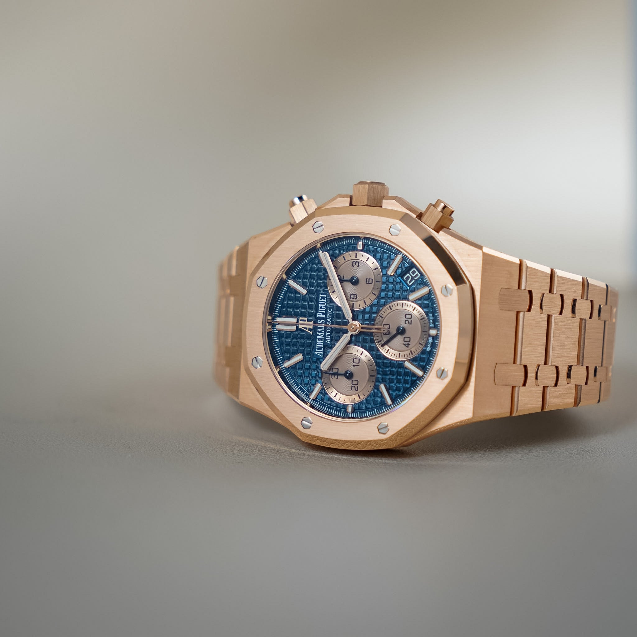 A luxury wristwatch with a rose gold-toned metal case and bracelet, featuring a textured blue dial with silver-toned subdials and markers.