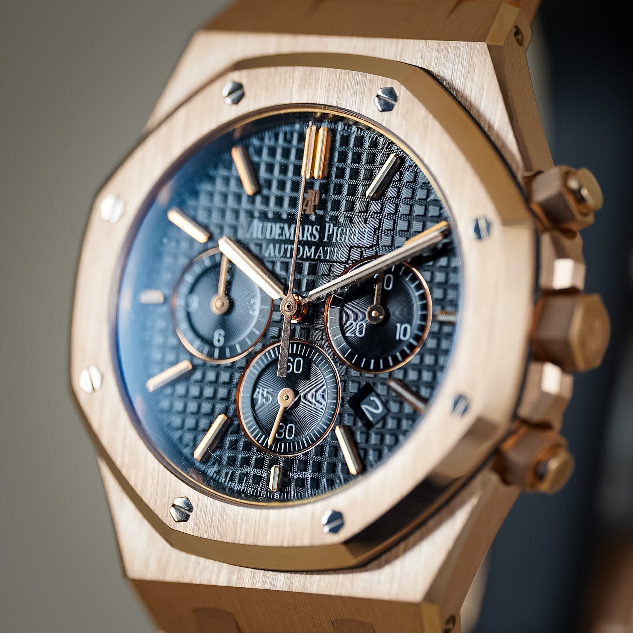 Close-up of an Audemars Piguet Royal Oak Automatic watch with a brushed rose gold-toned case, black textured dial, and black subdials.