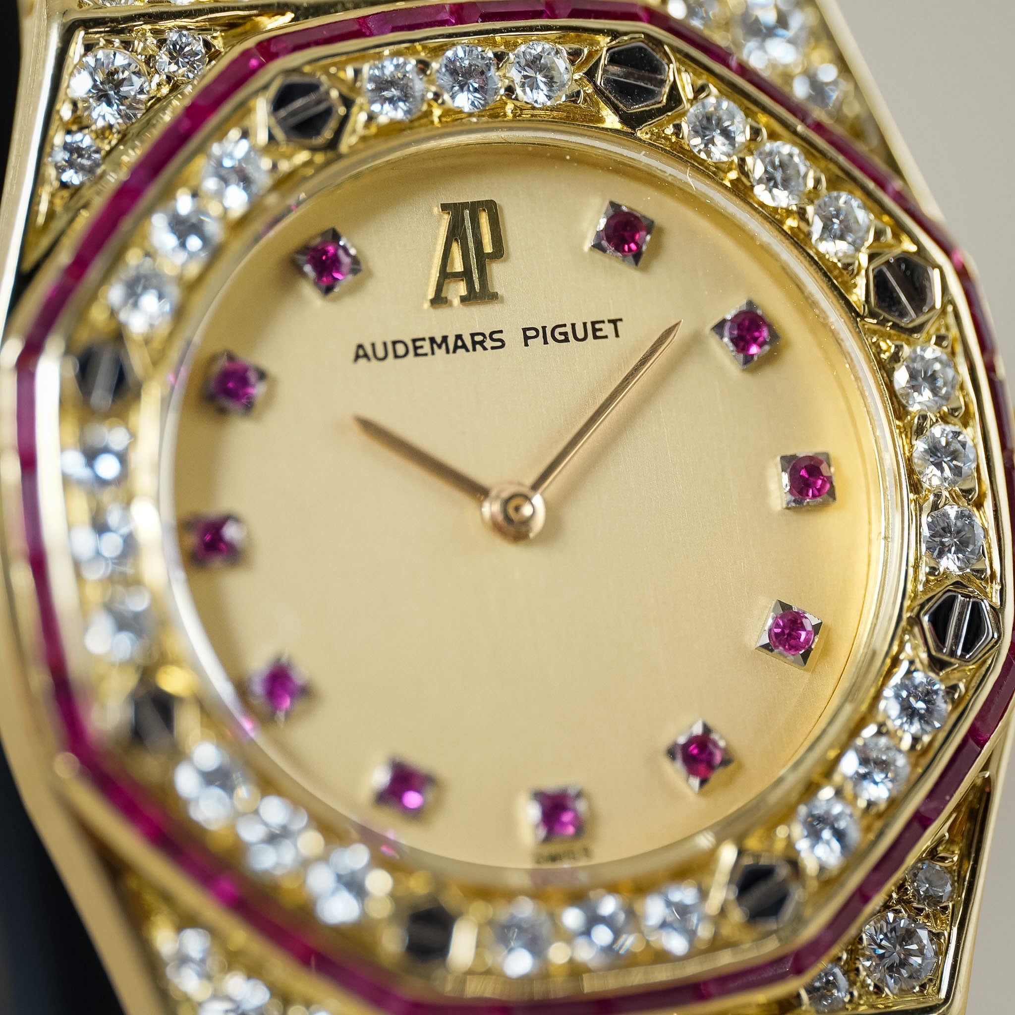 Close-up of an Audemars Piguet gold watch with a cream dial, pink ruby hour markers, and a bezel set with diamonds and pink rubies.