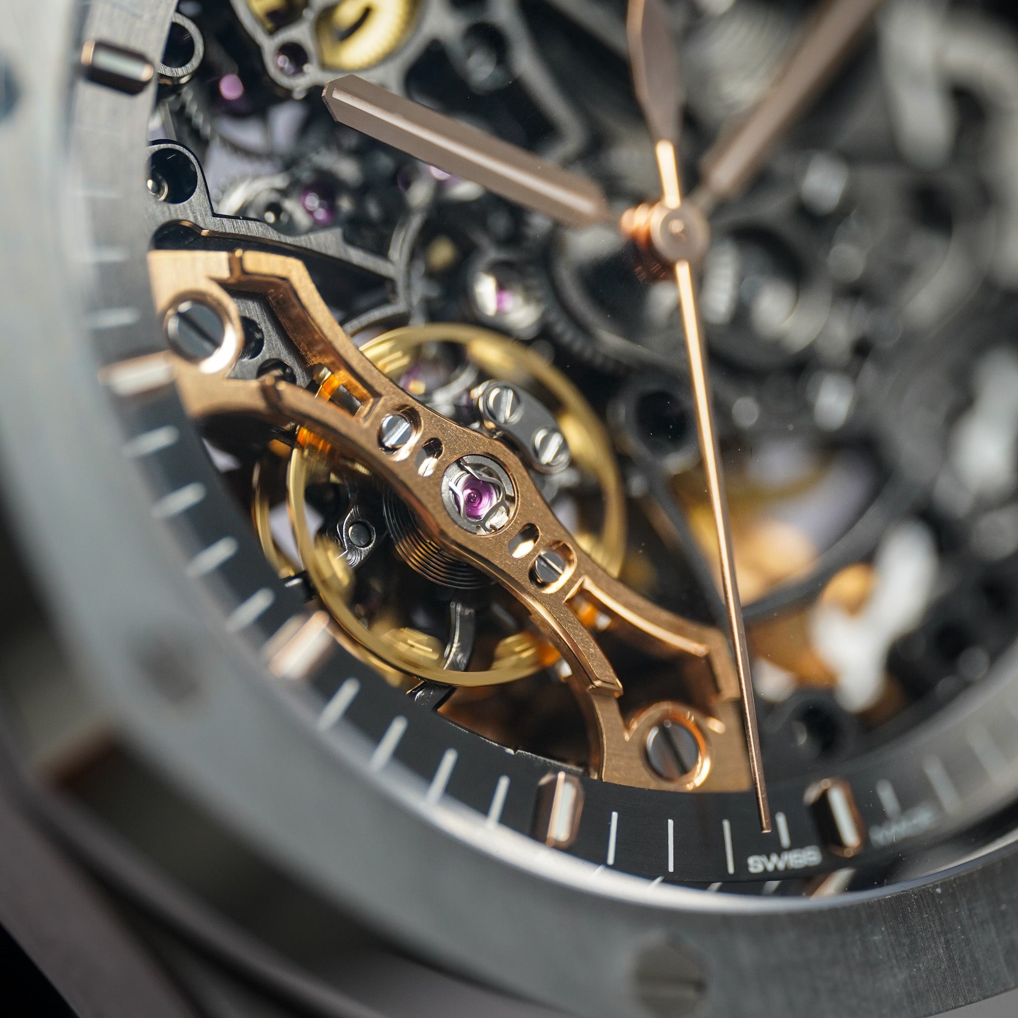 Extreme close-up of a skeleton watch dial showing intricate gold-toned and rose-gold mechanical gears, with a dark gray bezel and black watch face.