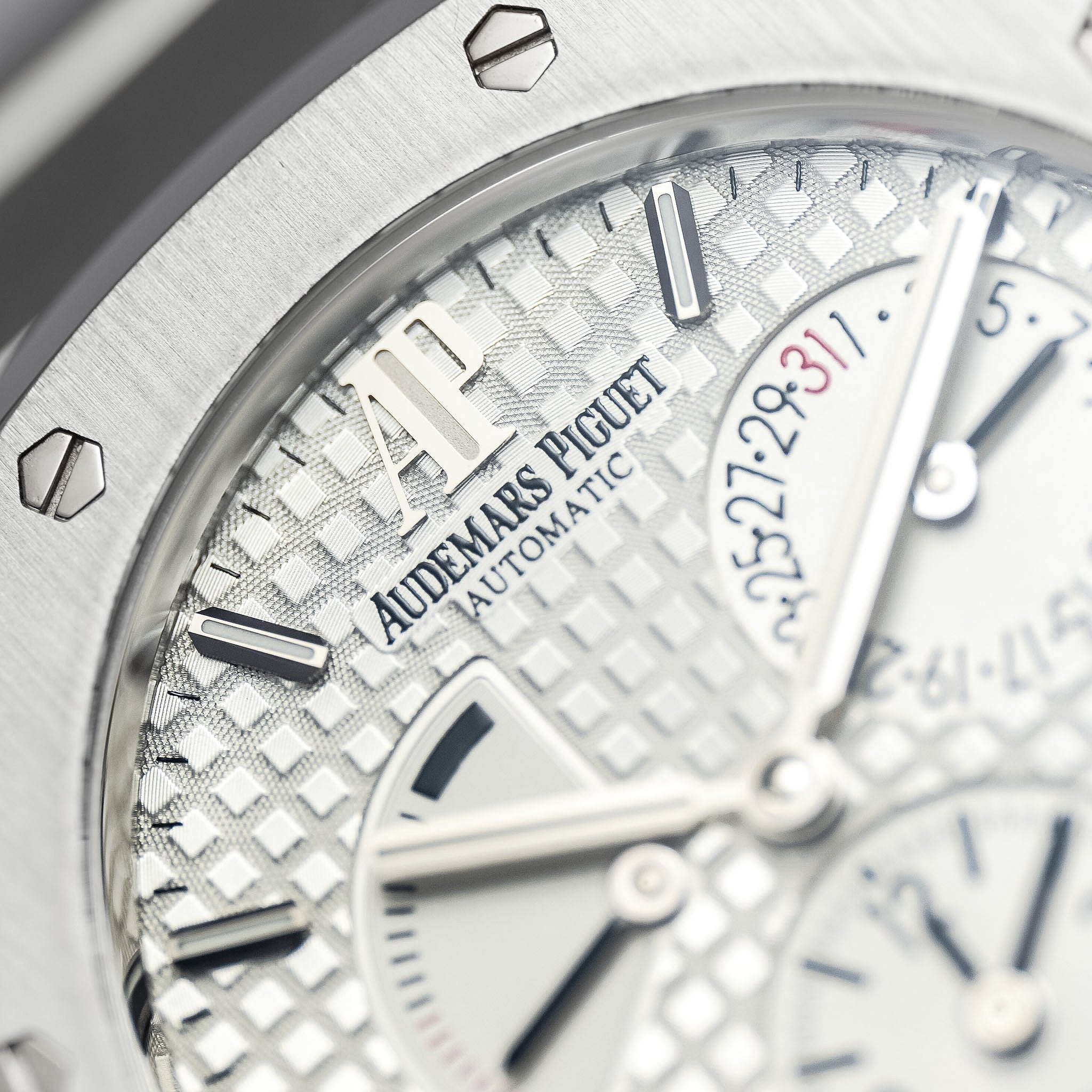 Close-up of an Audemars Piguet Automatic watch dial with a silver textured pattern, silver-tone hands and markers, and part of the stainless steel bezel visible.