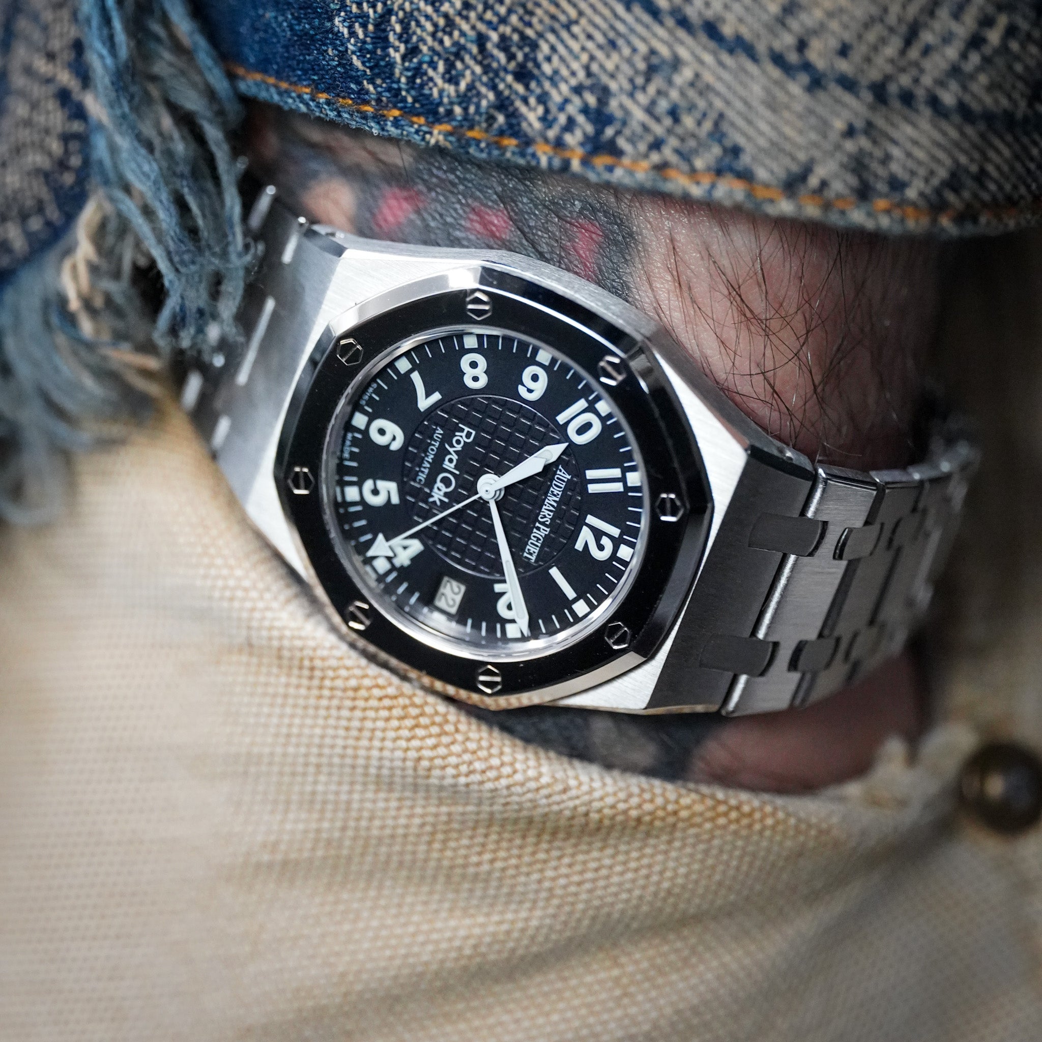 A close-up shot of a wrist wearing a silver-toned metal bracelet watch with a black dial and black bezel. The watch brand 'Topo' is visible on the dial.