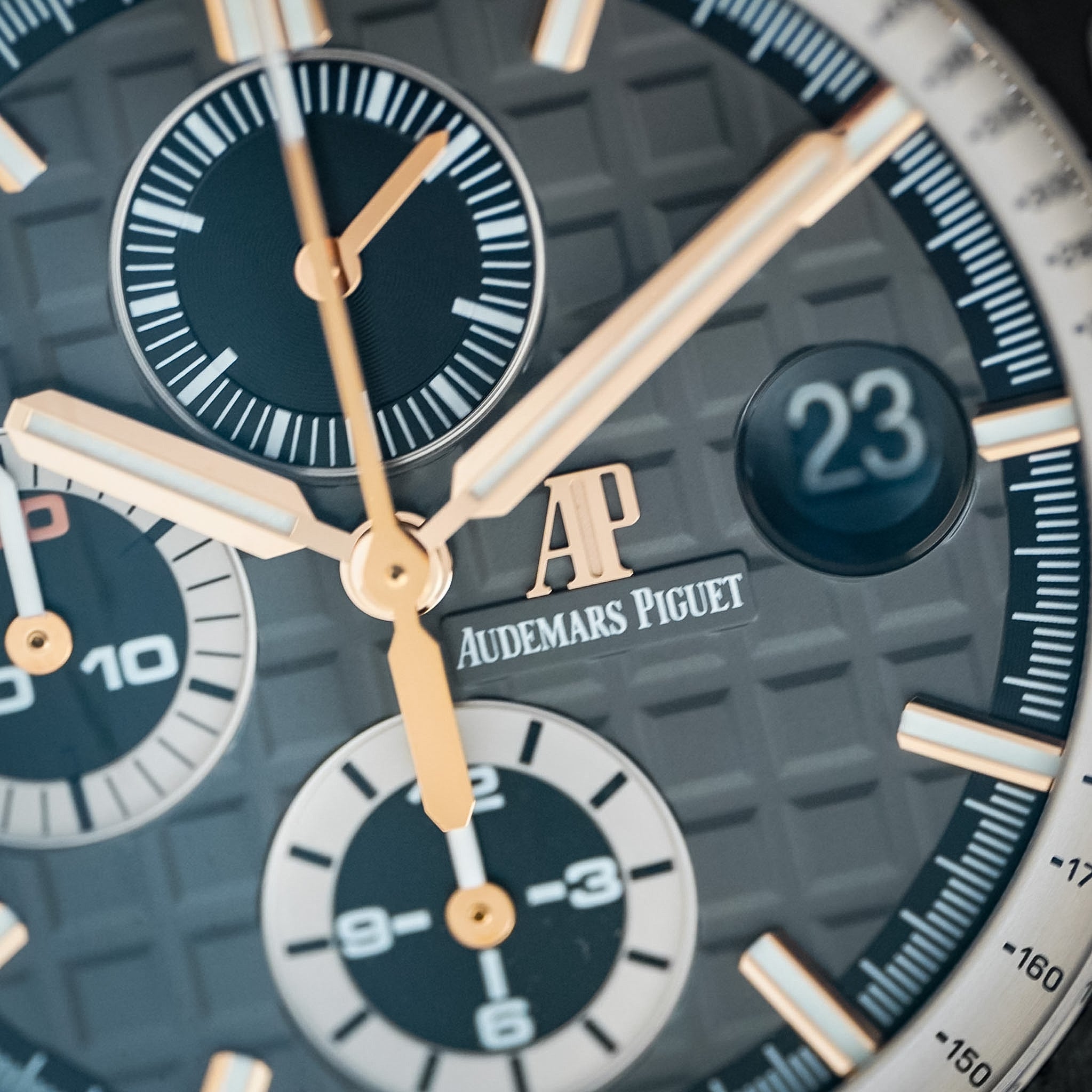 Close-up of an Audemars Piguet chronograph watch dial with a textured gray and black patterned case, gold-tone hands and markers, and white subdials.
