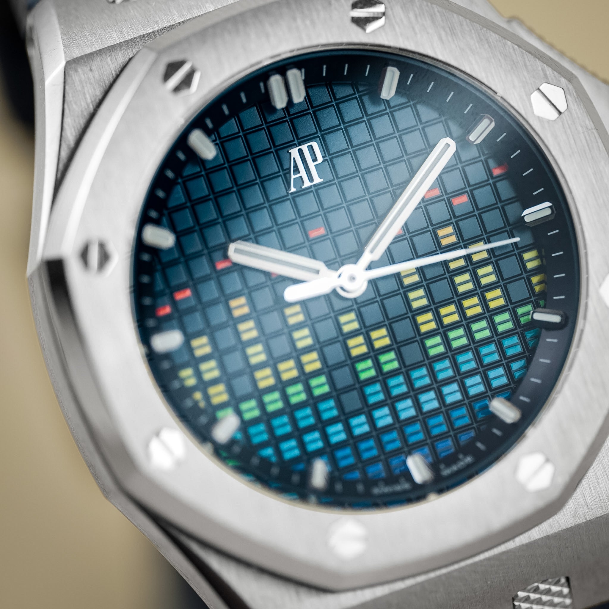 Close-up of a silver-toned wristwatch with an octagonal bezel and a blue grid dial featuring a multicolor audio-equalizer style graphic in blue, green, yellow, and red. The AP logo is visible on the dial.