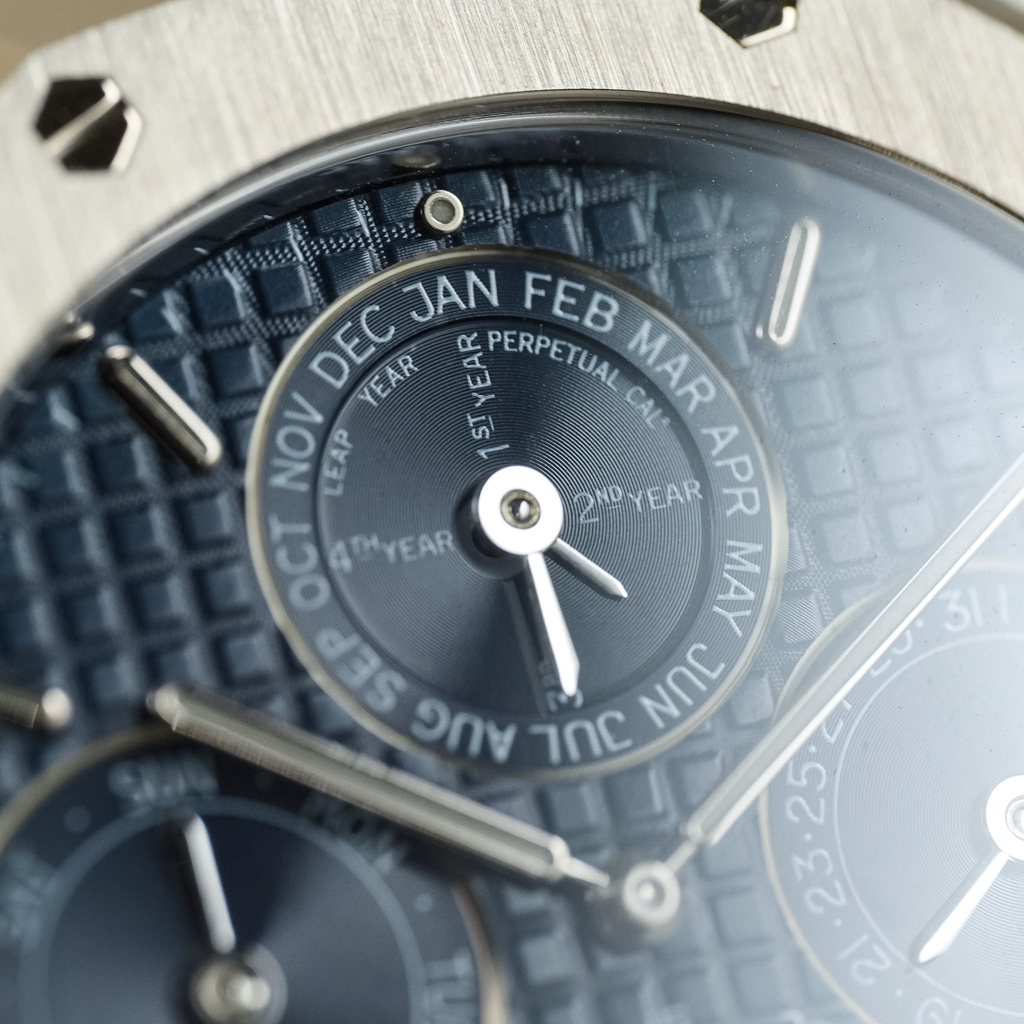 Close-up of a Perpetual Calendar watch dial with a textured blue and gray patterned face, silver bezel lugs, and white date hands.