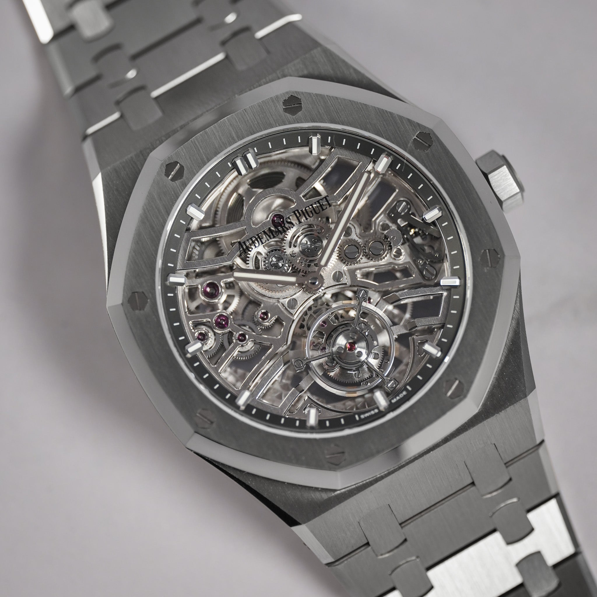 A close-up shot of a titanium skeleton watch with a brushed silver-gray case, a transparent dial showing the intricate mechanical movement, and a matching titanium link bracelet on a neutral gray background.