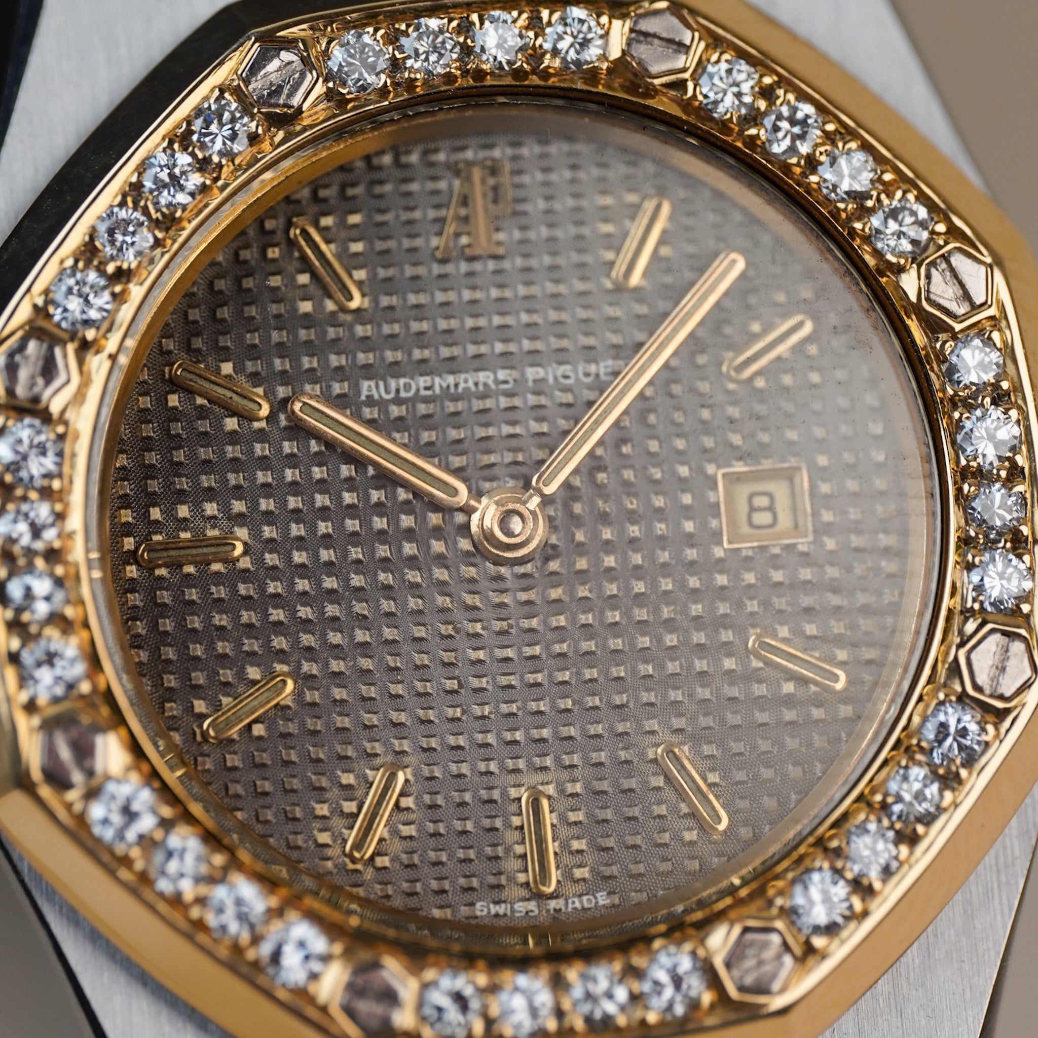 Close-up of an Audemars Piguet Royal Oak watch featuring a gold-toned octagonal bezel encrusted with diamonds, a textured gold dial, and gold-toned hour markers and hands.