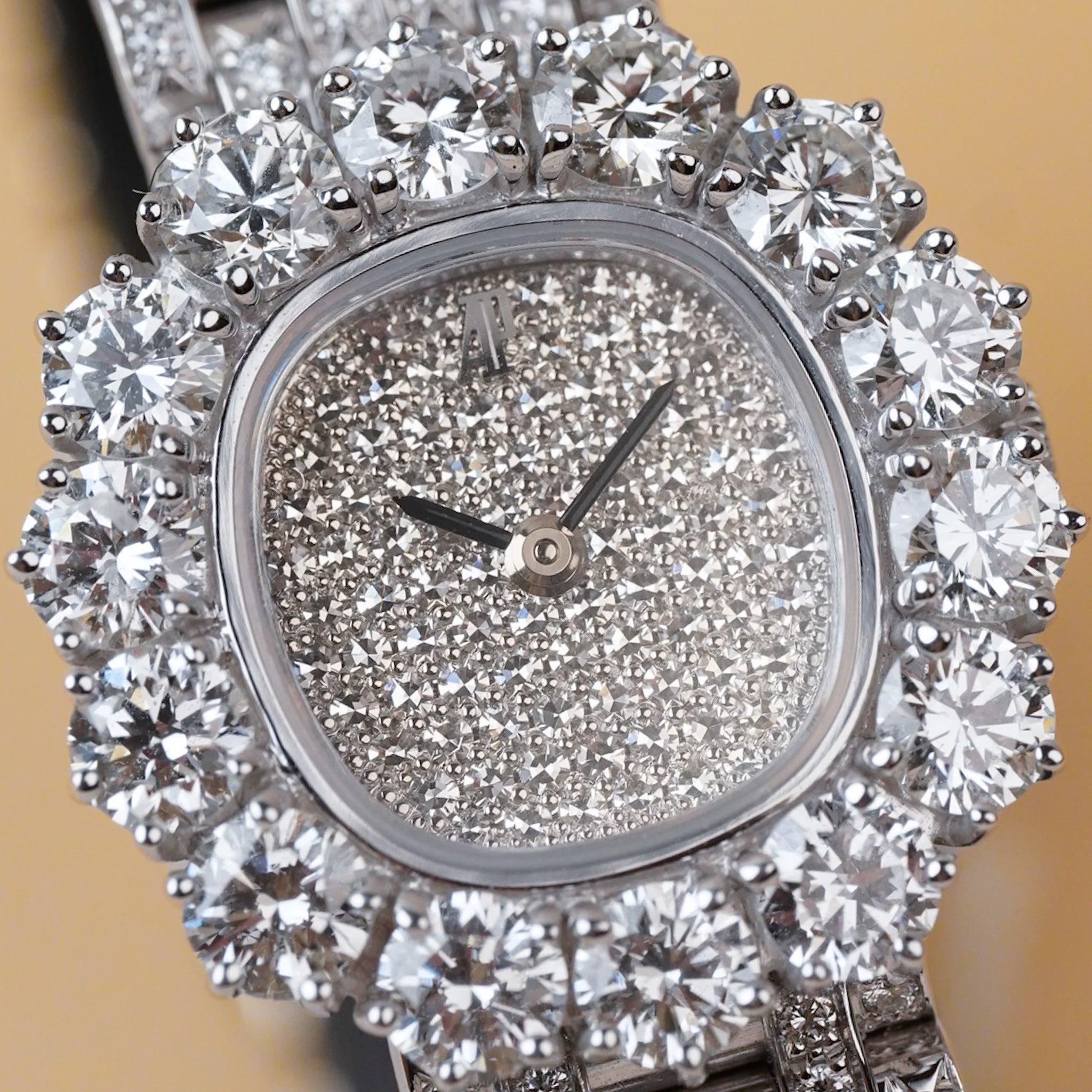 A luxury watch with a silver-toned case heavily encrusted with clear round diamonds, featuring a sparkling diamond-encrusted dial with silver hands.