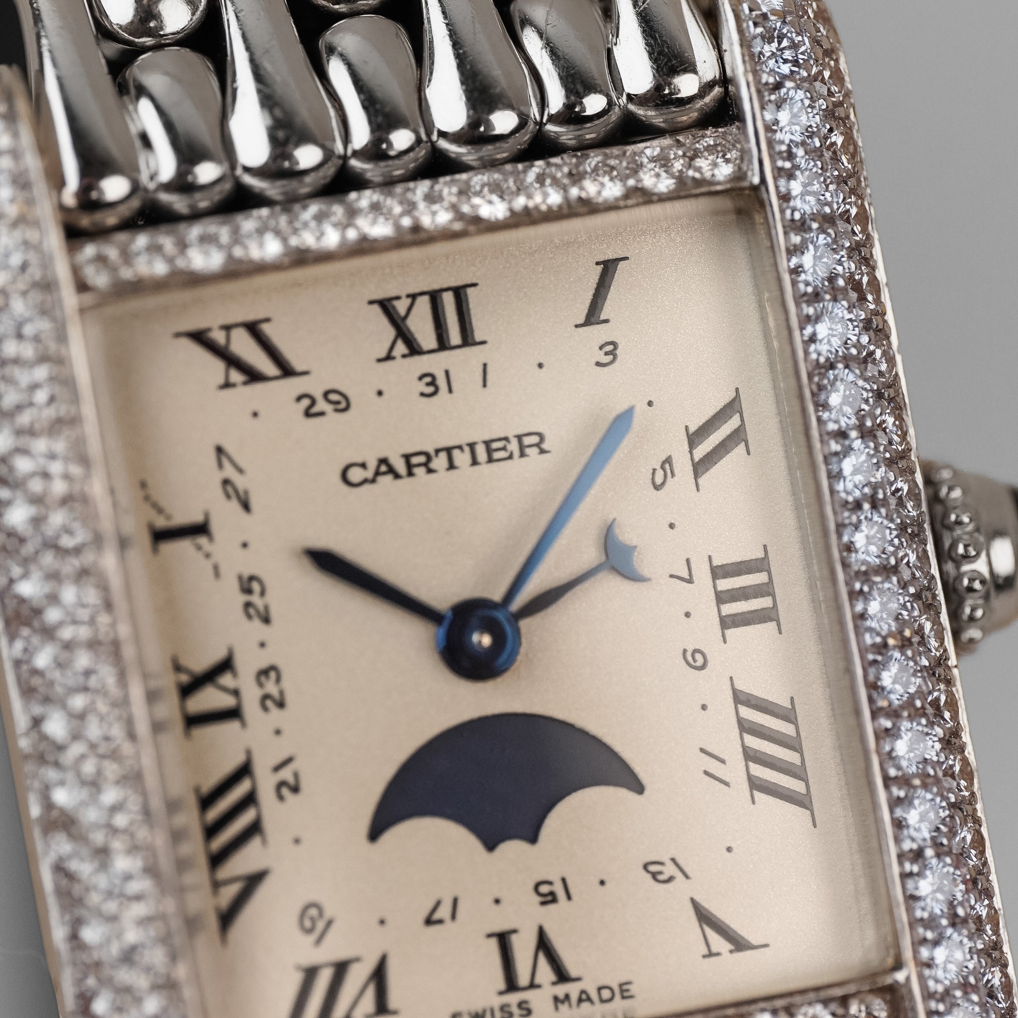 Closeup of a white gold Cartier Tank with white dial, Roman numerals, a moonphase indicator, and diamond bezel.
